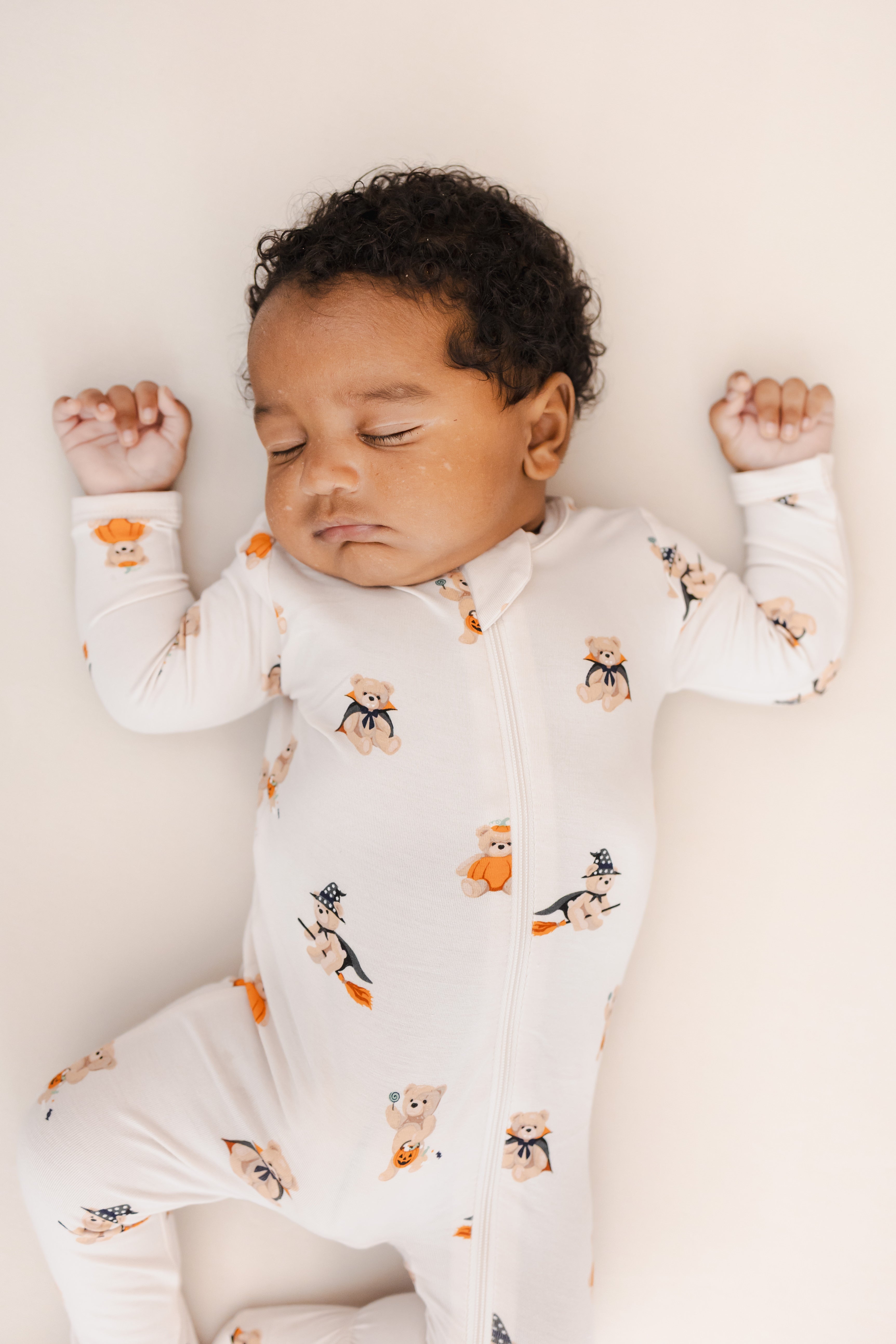 Baby sleeping in Zippered Footie in Halloween Teddy print on a beige background