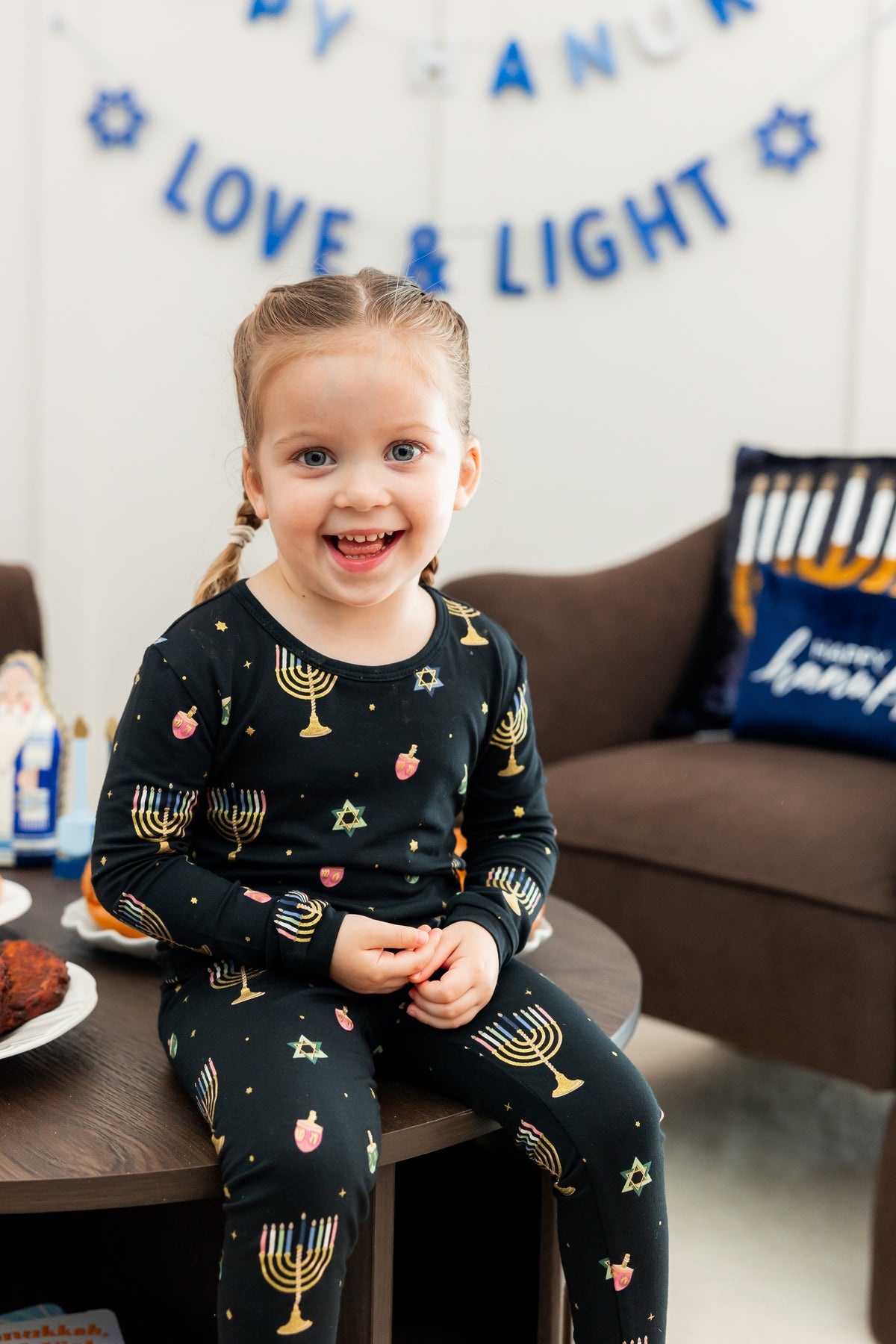 Toddler girl sitting on a table smiling in long sleeve hanukkah pajamas