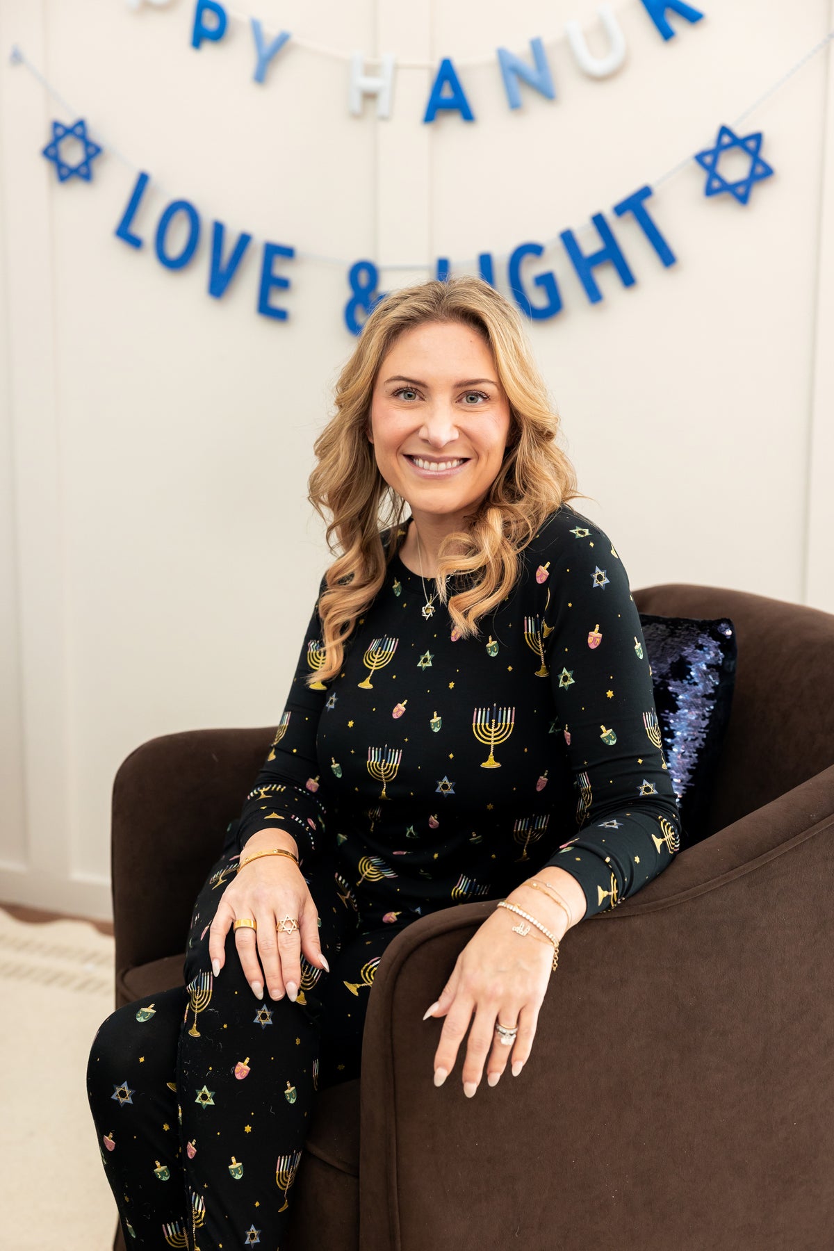 Woman sitting on a chair with her arm over the side smiling in hanukkah jogger pajamas