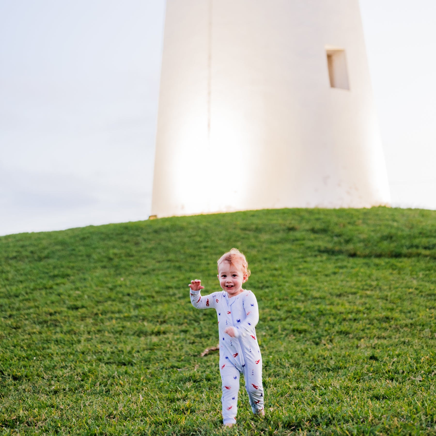 Toddler running on a hill wearing Zippered Romper in Harbor with a lighthouse in the background