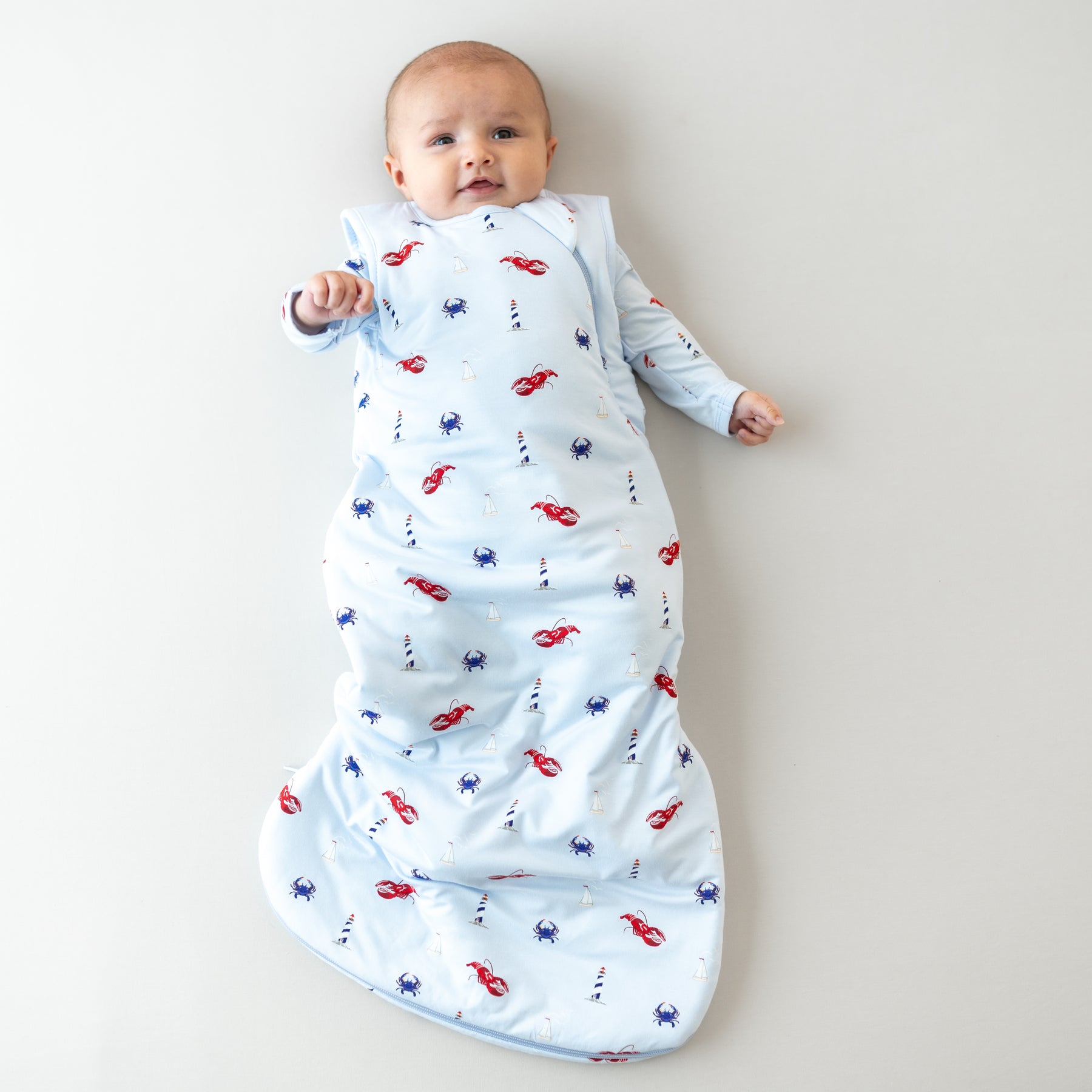 Infant laying down wearing the Sleep Bag in Harbor 1.0 with matching long sleeve romper