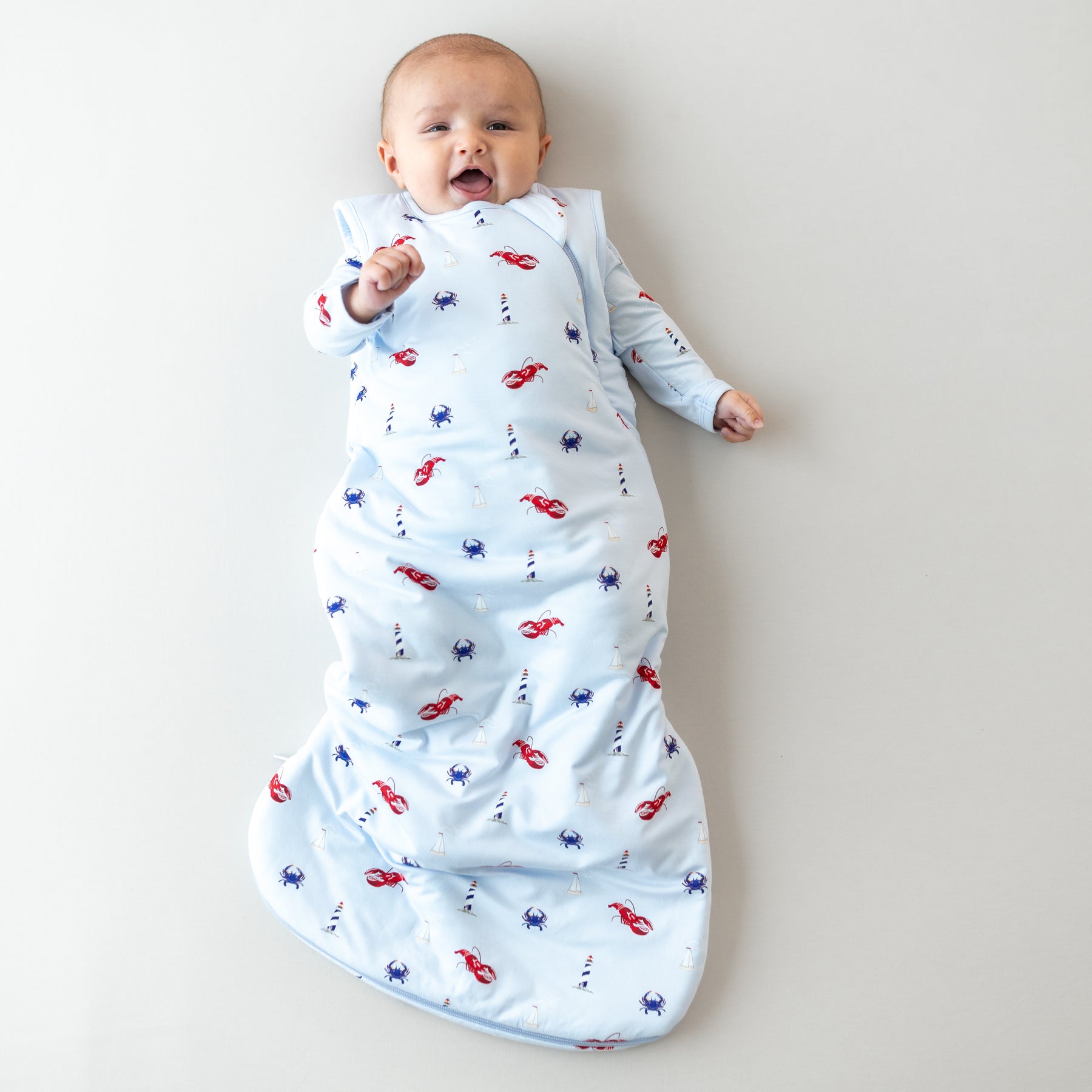 Smiling baby laying down wearing the Sleep Bag in Harbor 1.0 with matching long sleeve romper