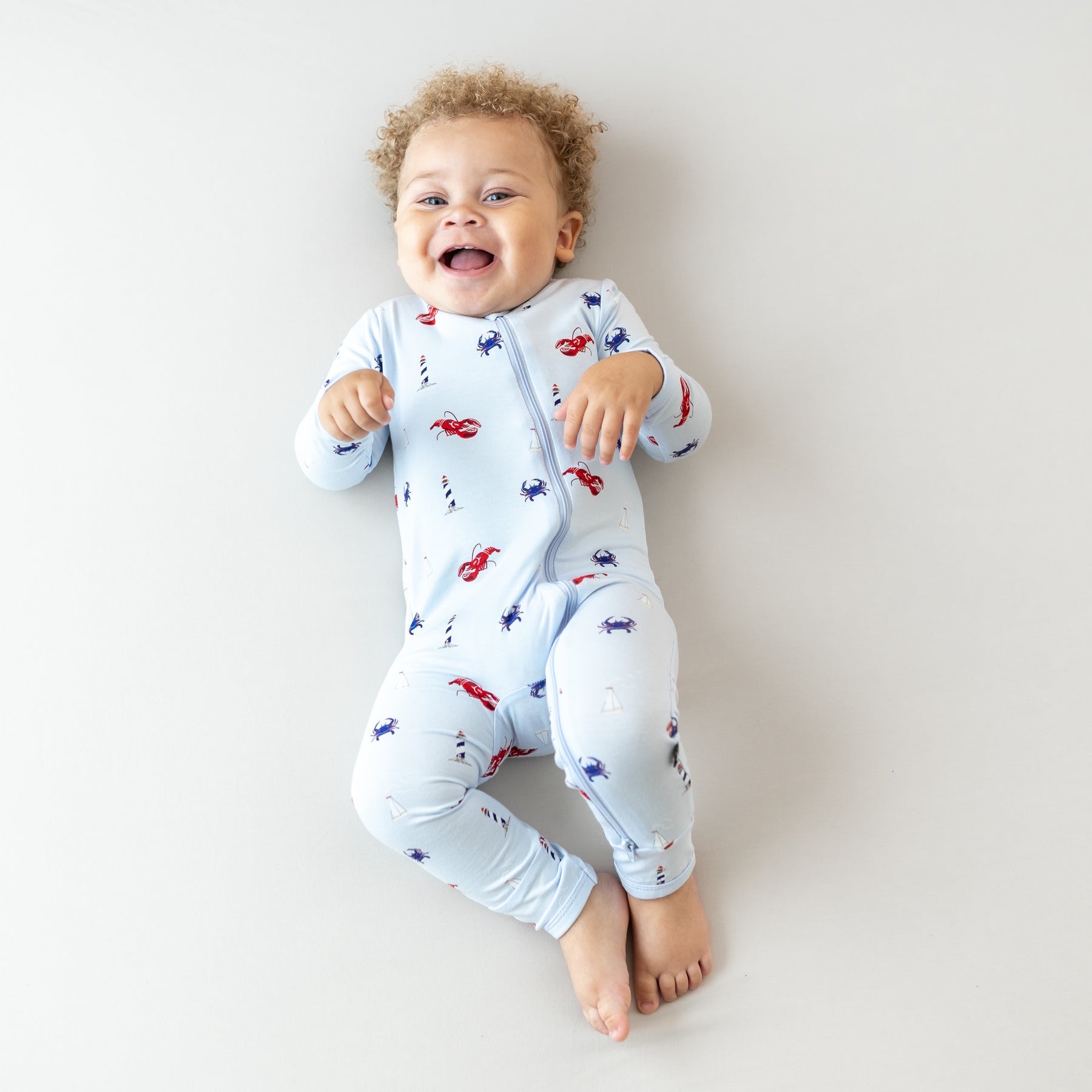 Smiling infant laying down wearing the Zippered Romper in Harbor