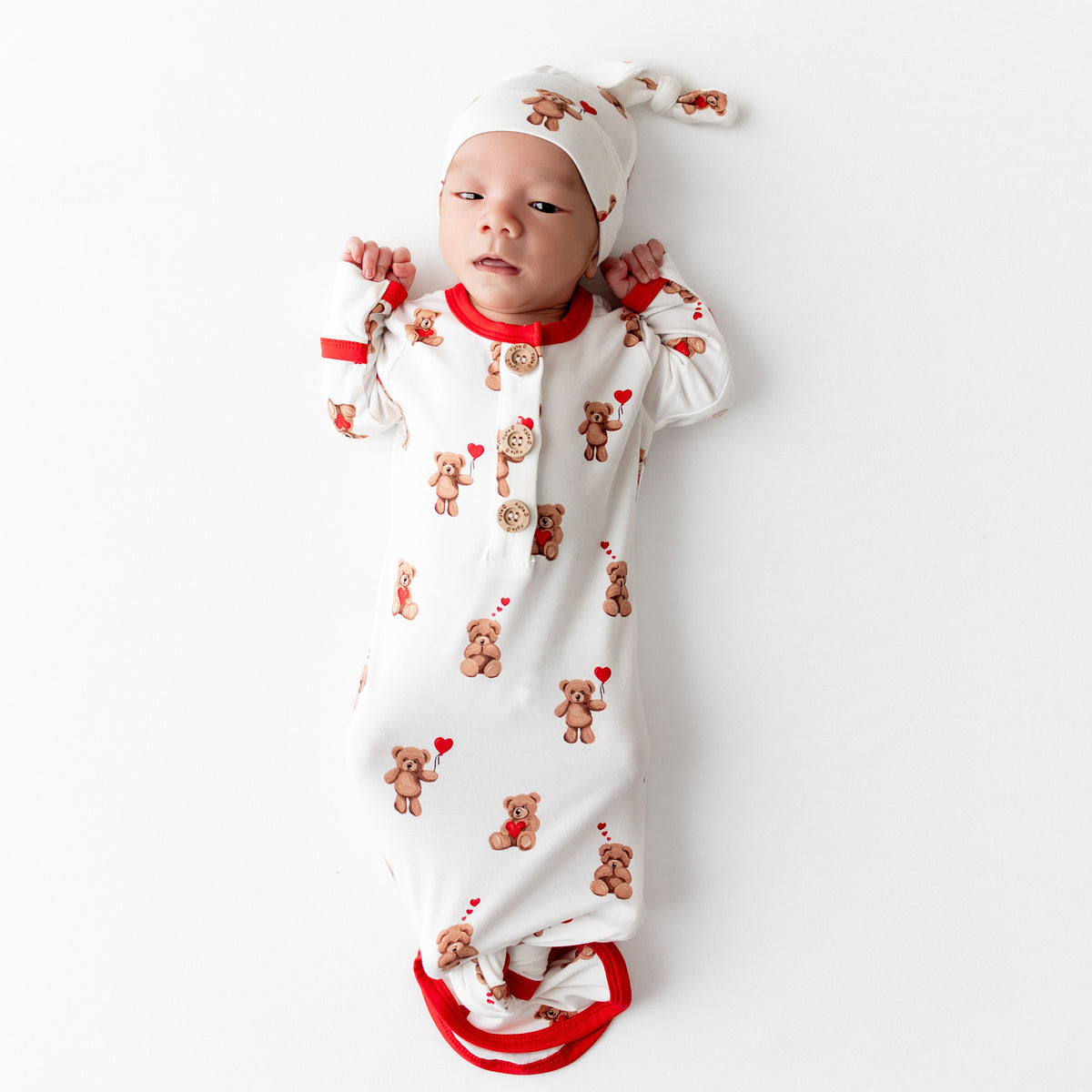 Newborn laying on a white surface wearing the soft Knotted Gown with Hat Set in Bear Hearts