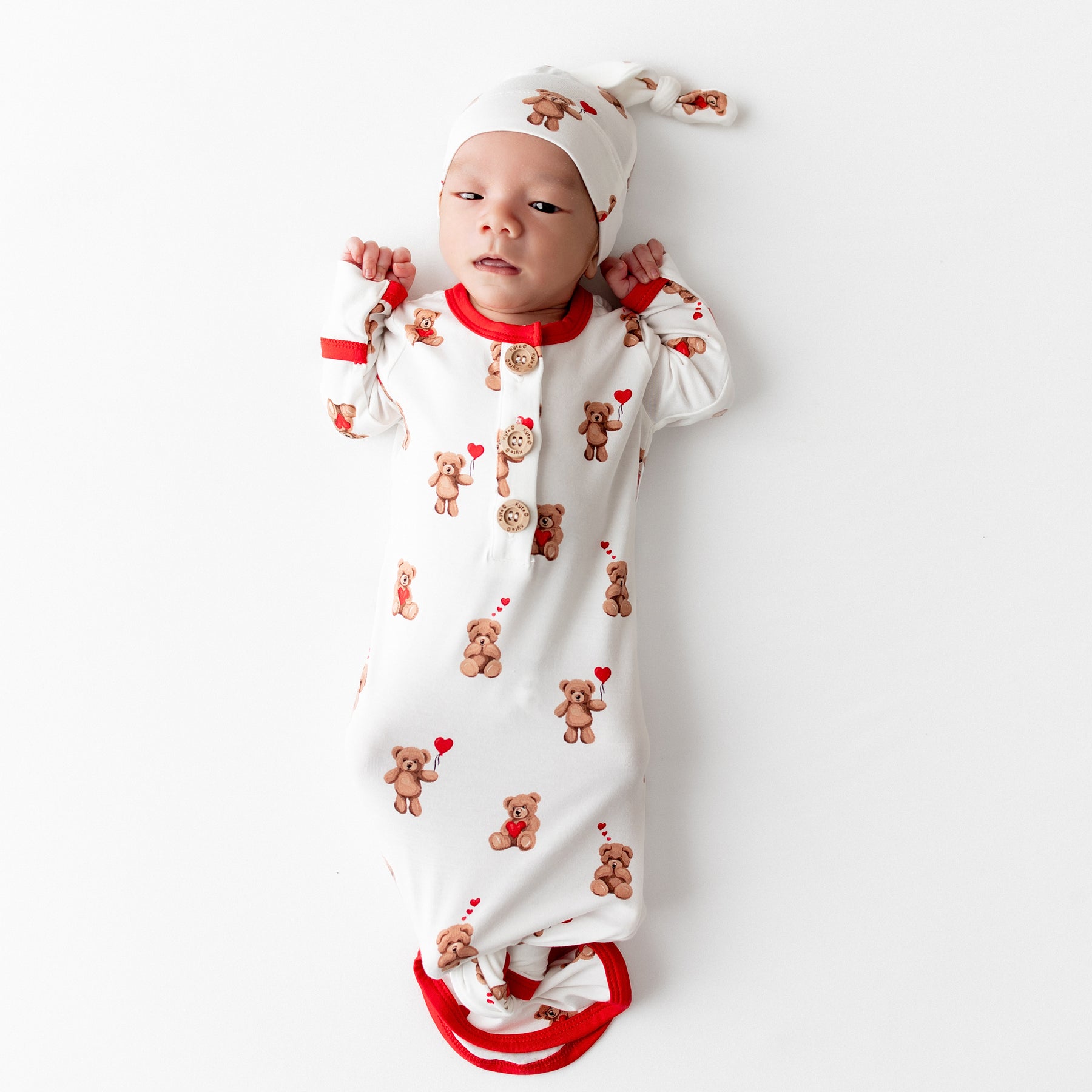 Newborn laying on a white surface wearing the soft Knotted Gown with Hat Set in Bear Hearts