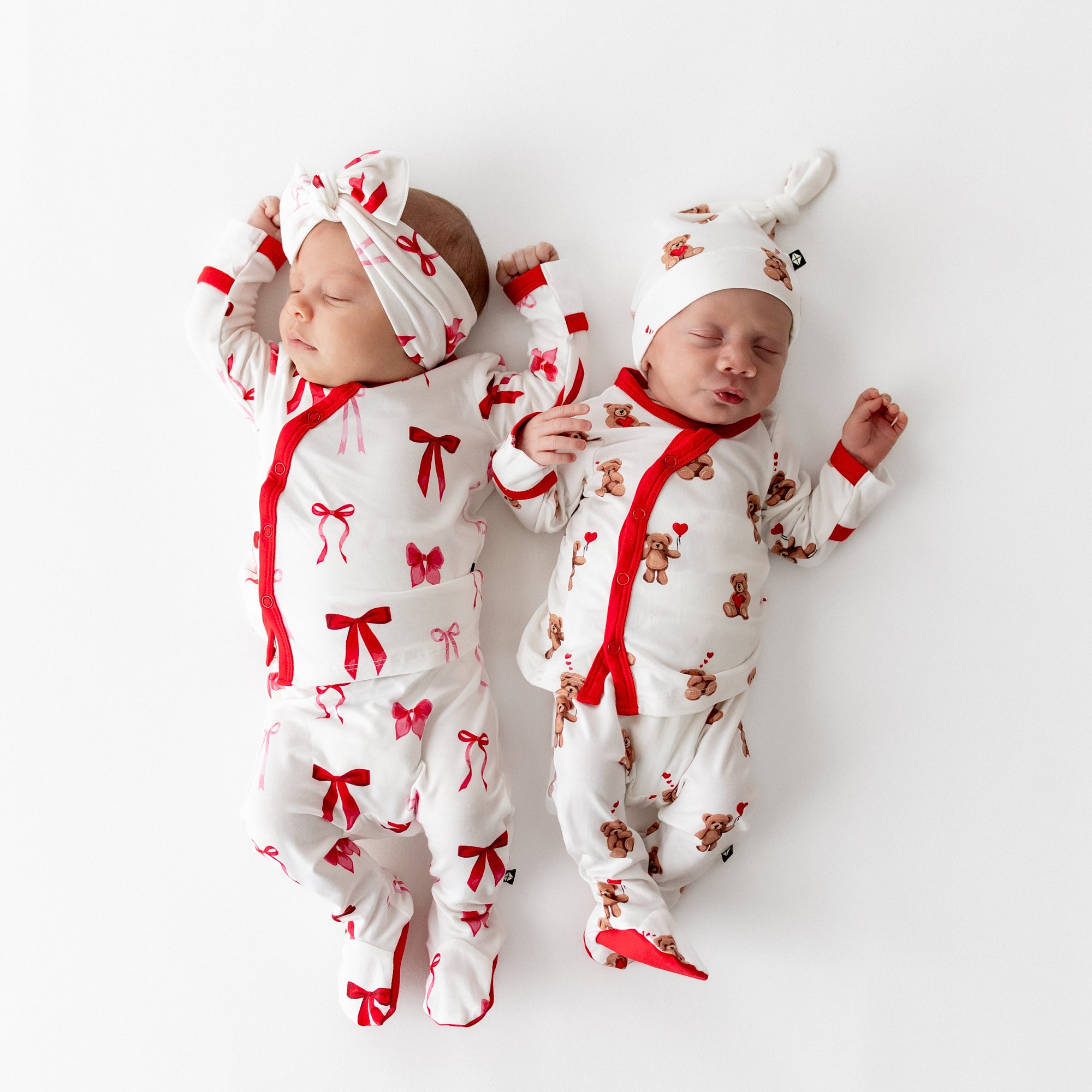 Two sleeping newborns laying side by side wearing the Take Me Home Set with Cap in Bear Hearts and Take me Home Set with Bow in Small Love Bow