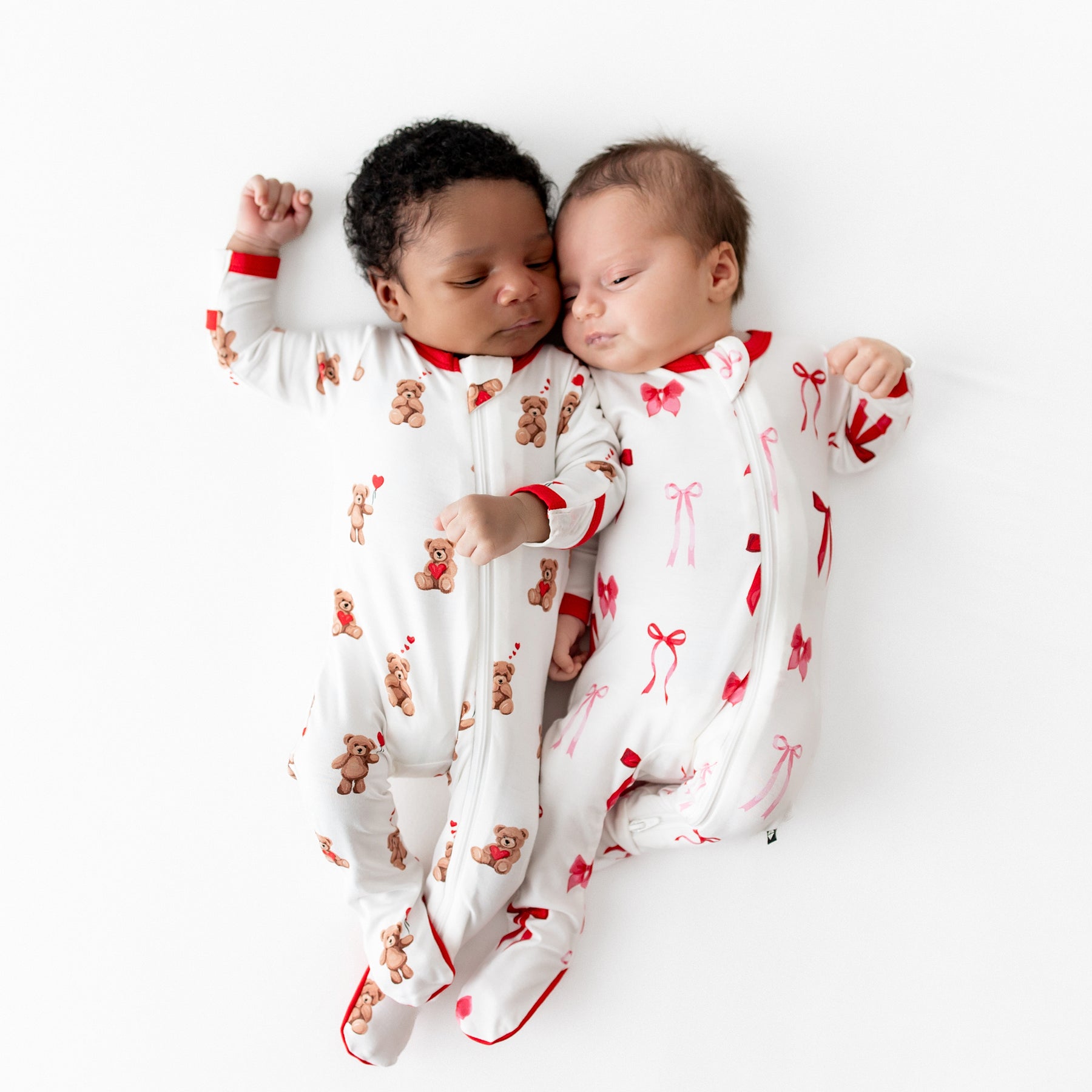 Two newborns laying side by side wearing zippered footies in Bear hearts and Small Love Bow