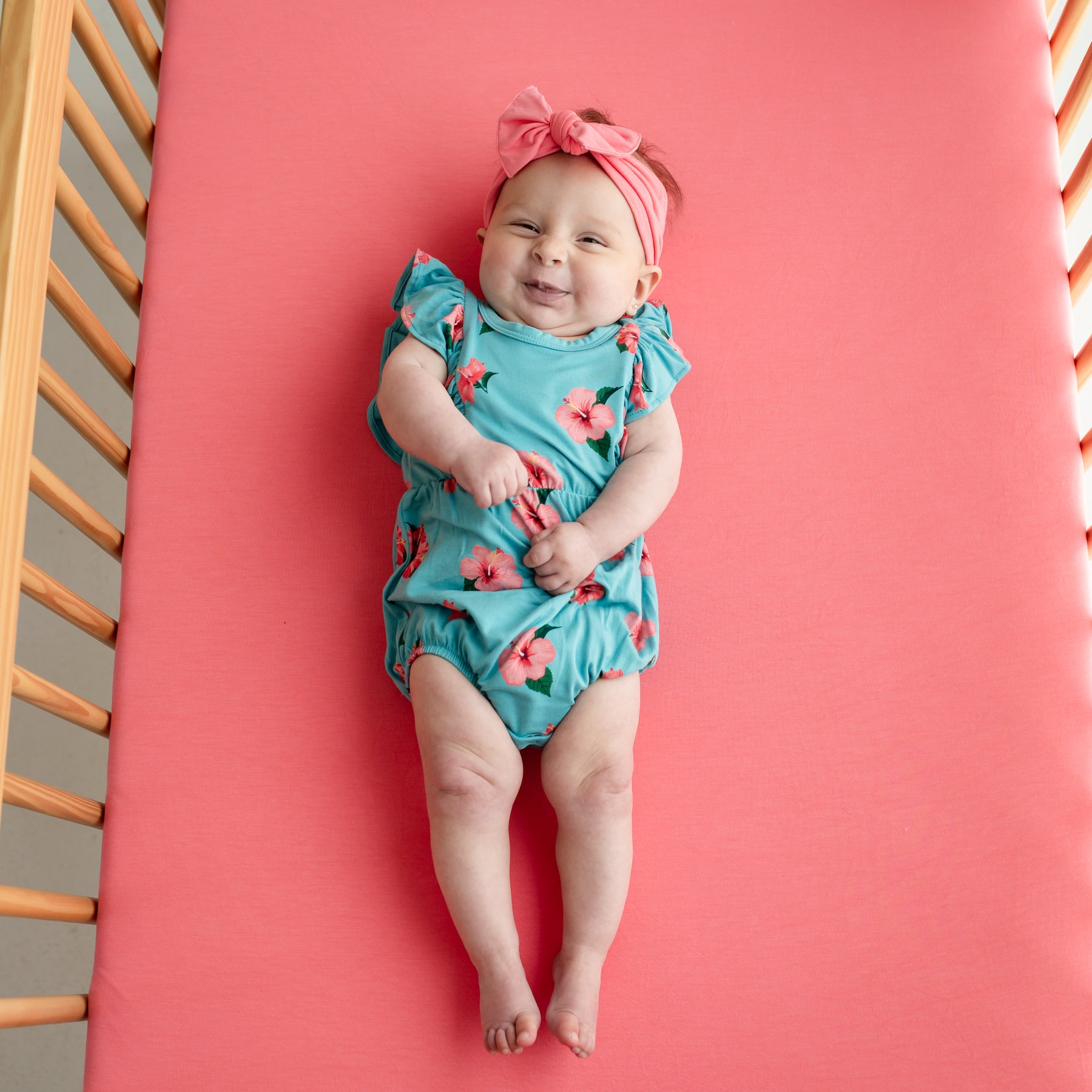 Baby laying wearing Kyte Baby Bubble Romper in Hibiscus