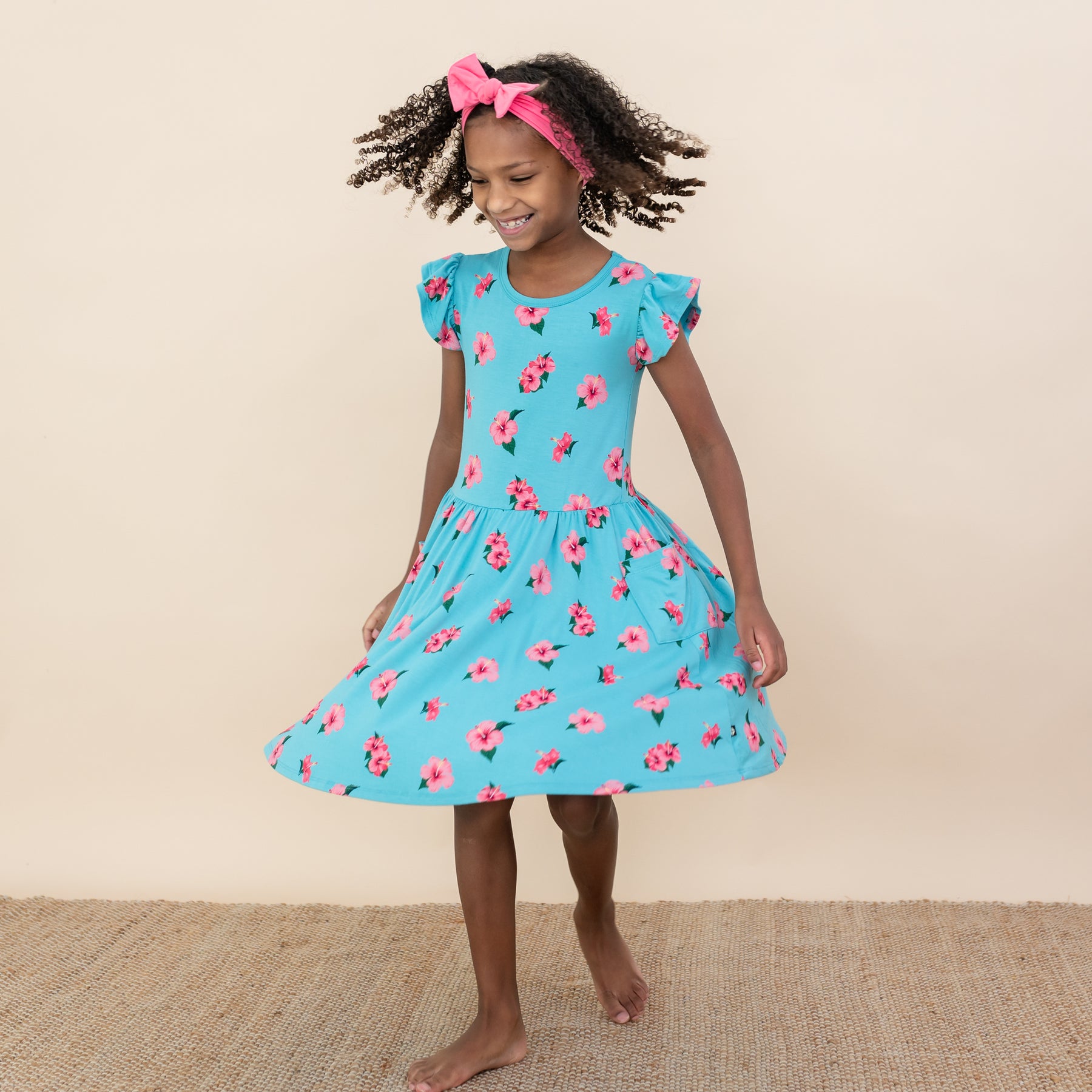 Child twirling in Kyte Pocket Dress in Hibiscus with Guava Bow