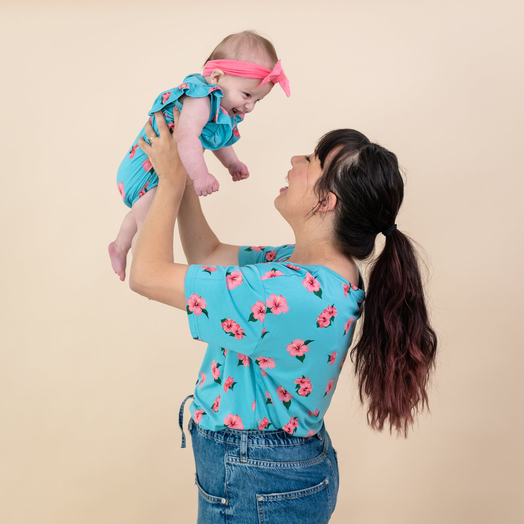 Woman wearing Kyte Hibiscus relaxed fit v-neck tee holding baby in matching Hibiscus bubble romper