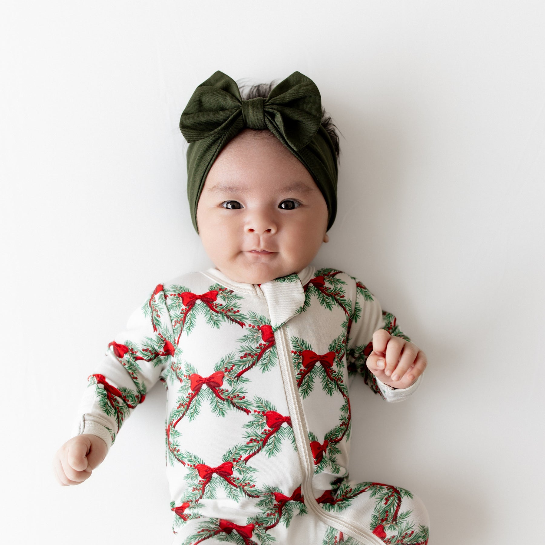 Close up of an infant wearing the Zippered Footie in Holiday Bow and a Fir Bow headband