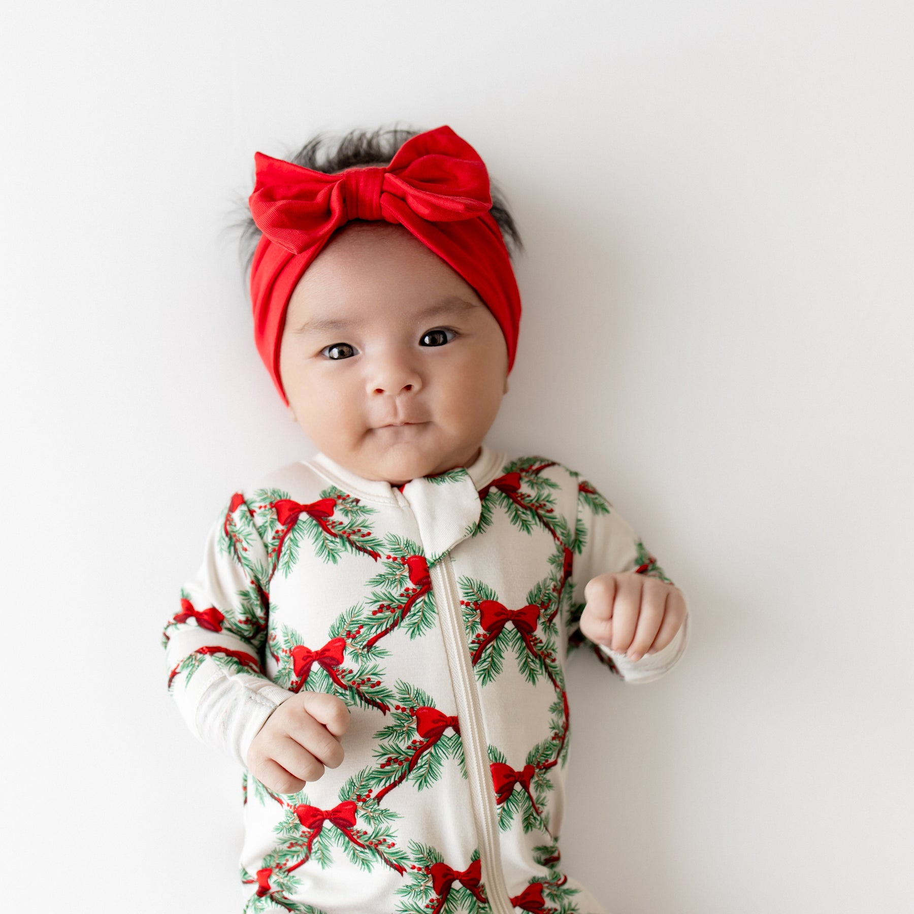 Close up of an infant wearing the Zippered Footie in Holiday Bow with a Cardinal bow Headband