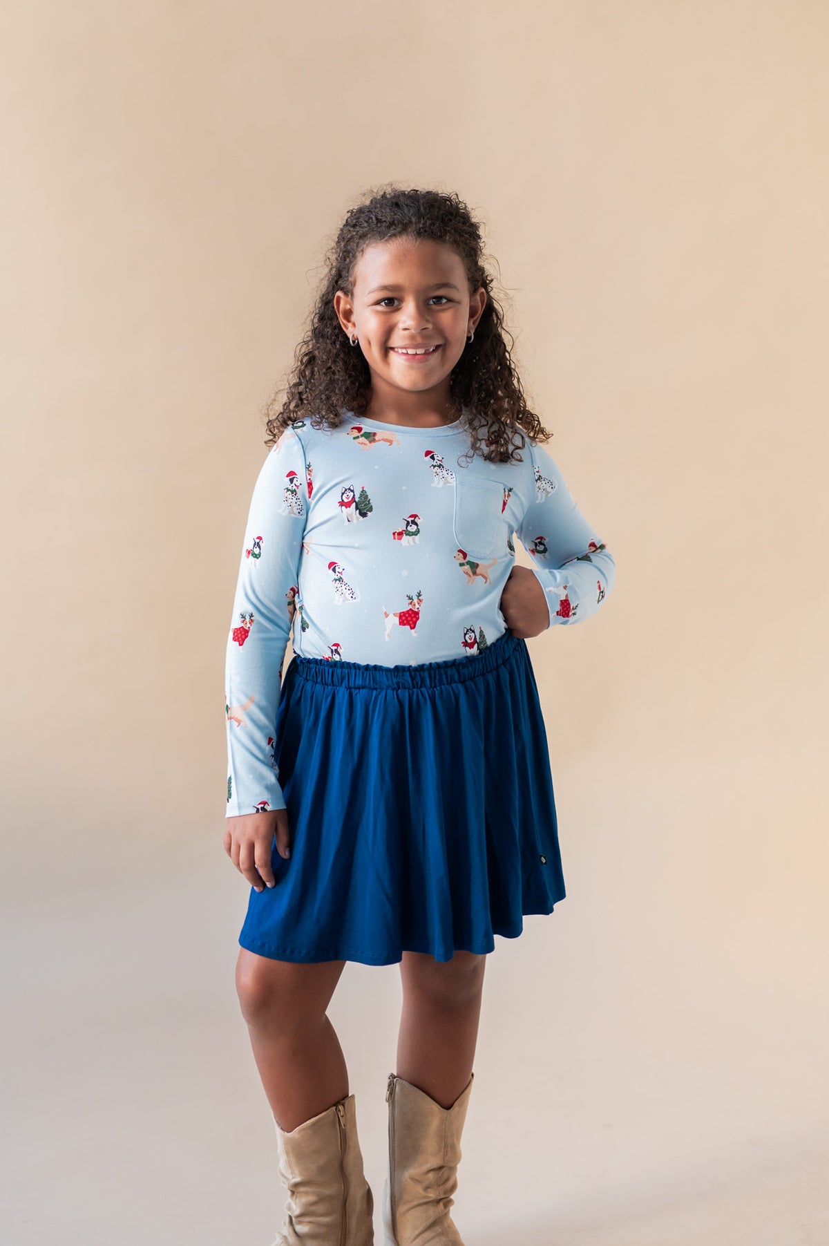 A girl smiling with her hand on her hip wearing a long sleeve crew neck tee in hanukkah print tucked into a blue skirt with cowboy boots