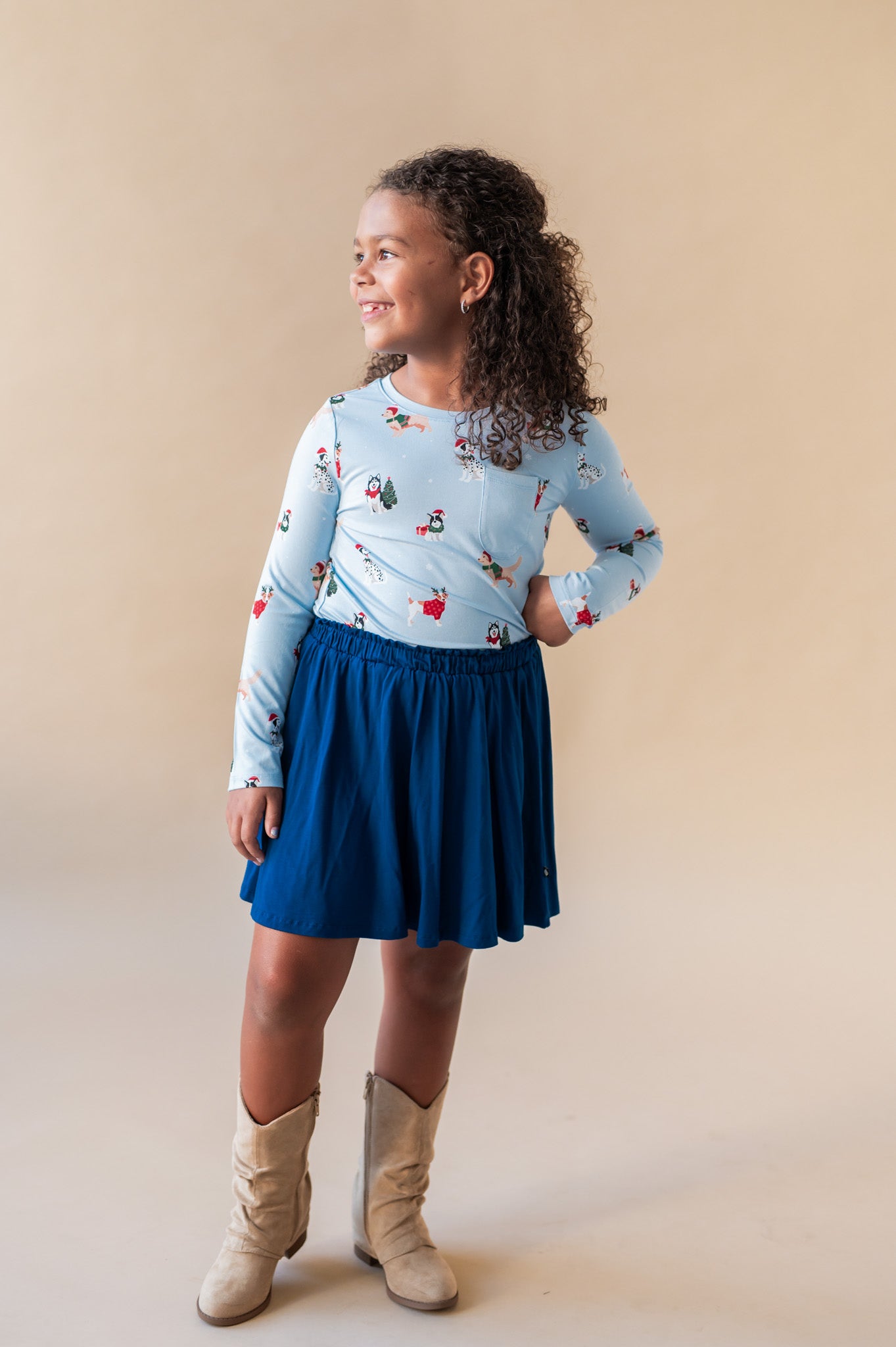 A girl smiling looking over her shoulder with her hand on her hip wearing a long sleeve crew neck tee in hanukkah print tucked into a blue skirt with cowboy boots