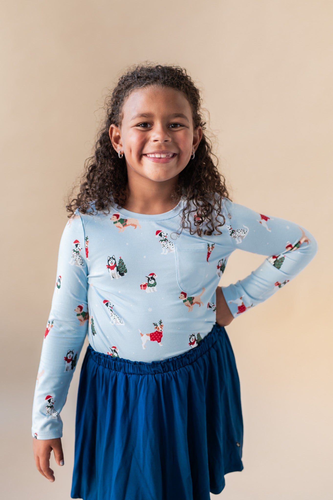 Girl smiling with her hand on her hip wearing a long sleeve crew neck tee in holiday ups tucked into a blue skirt