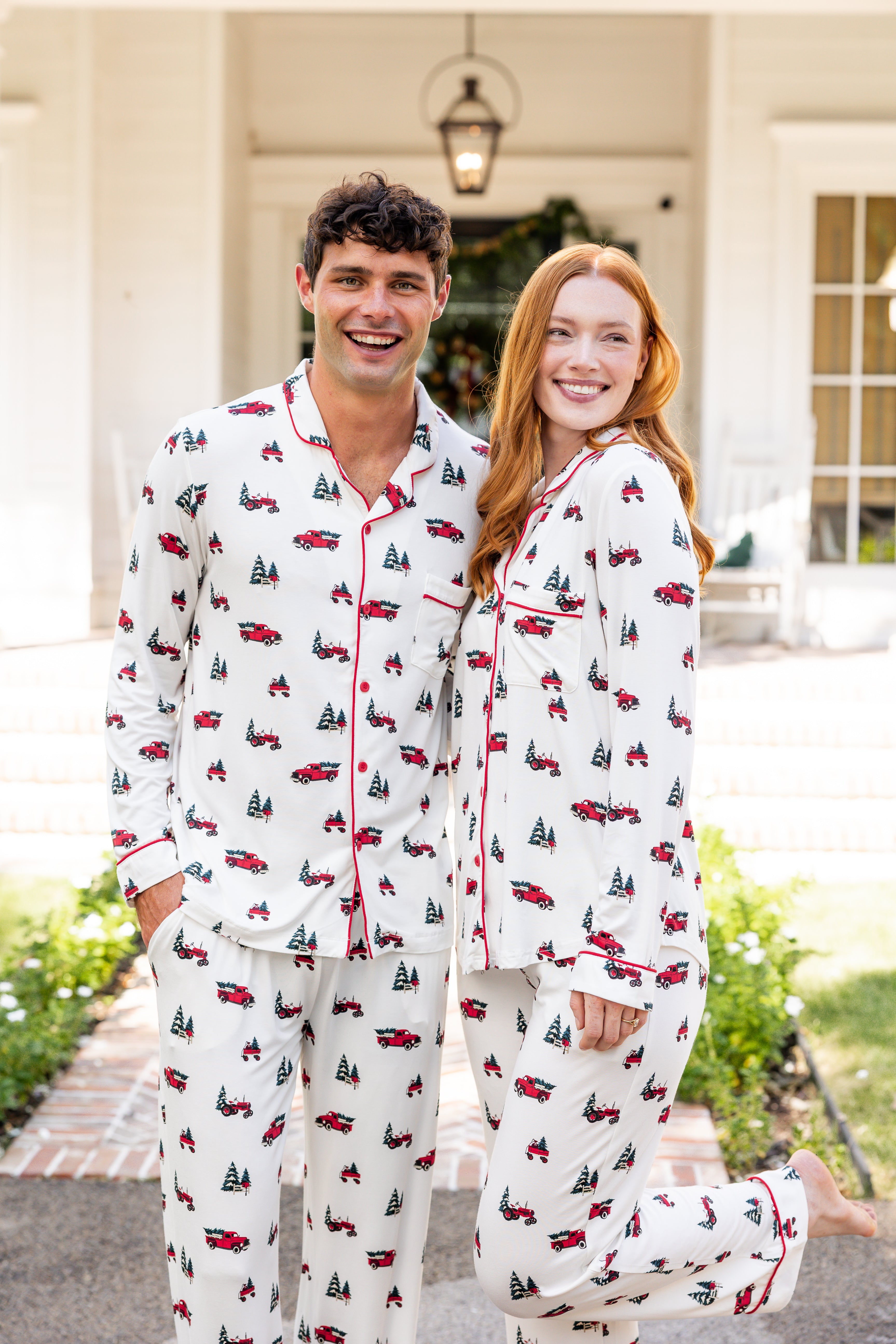 Man and woman wearing matching long sleeve pajama set in holiday tree farm print standing outdoors together