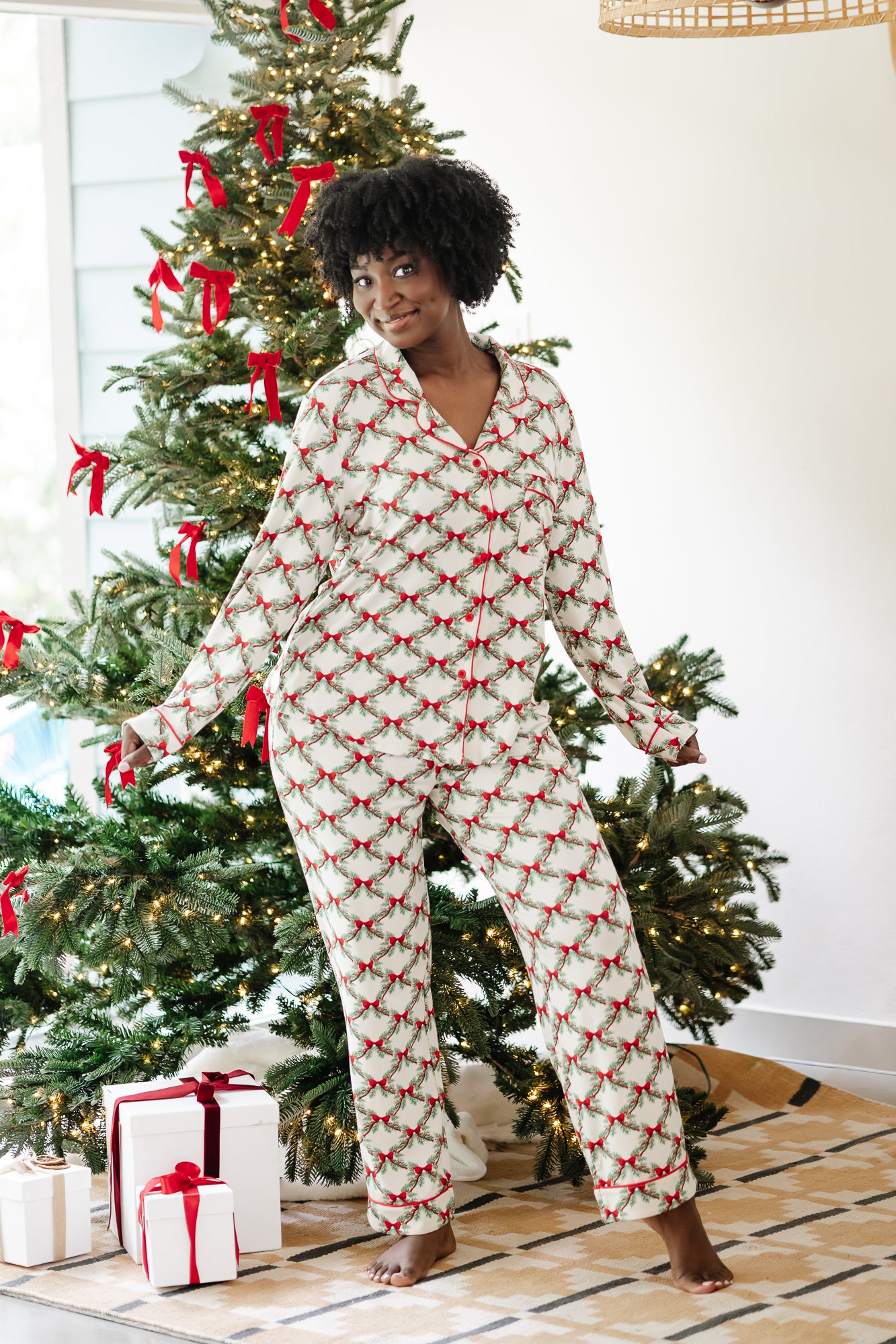 Female modeling the Long-Sleeved Women's Pajama Set in Holiday Bow standing in front of a decorated Christmas tree