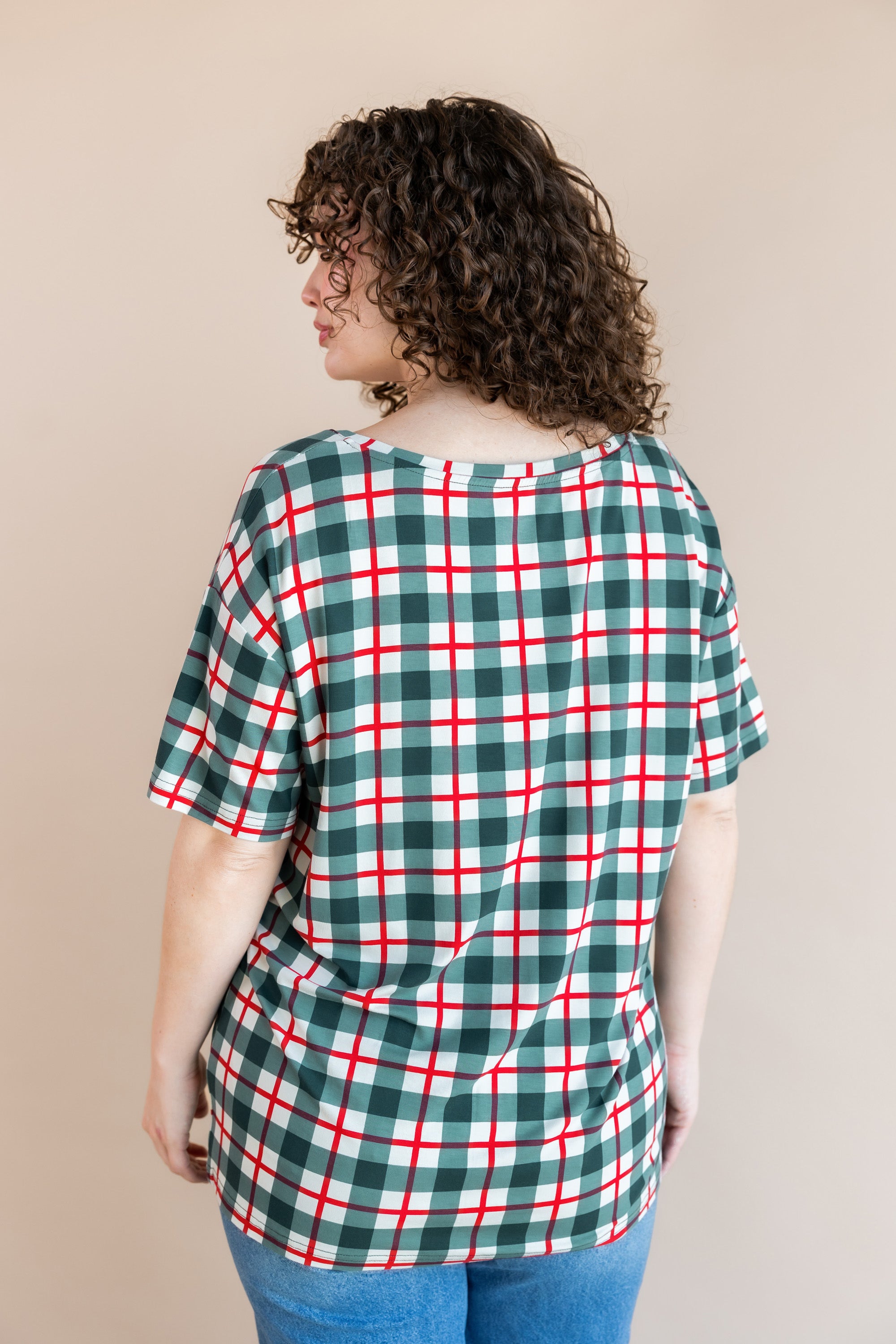 Back side of Modal wearing women's V-Neck Tee in Holiday Plaid over blue jeans on a beige background