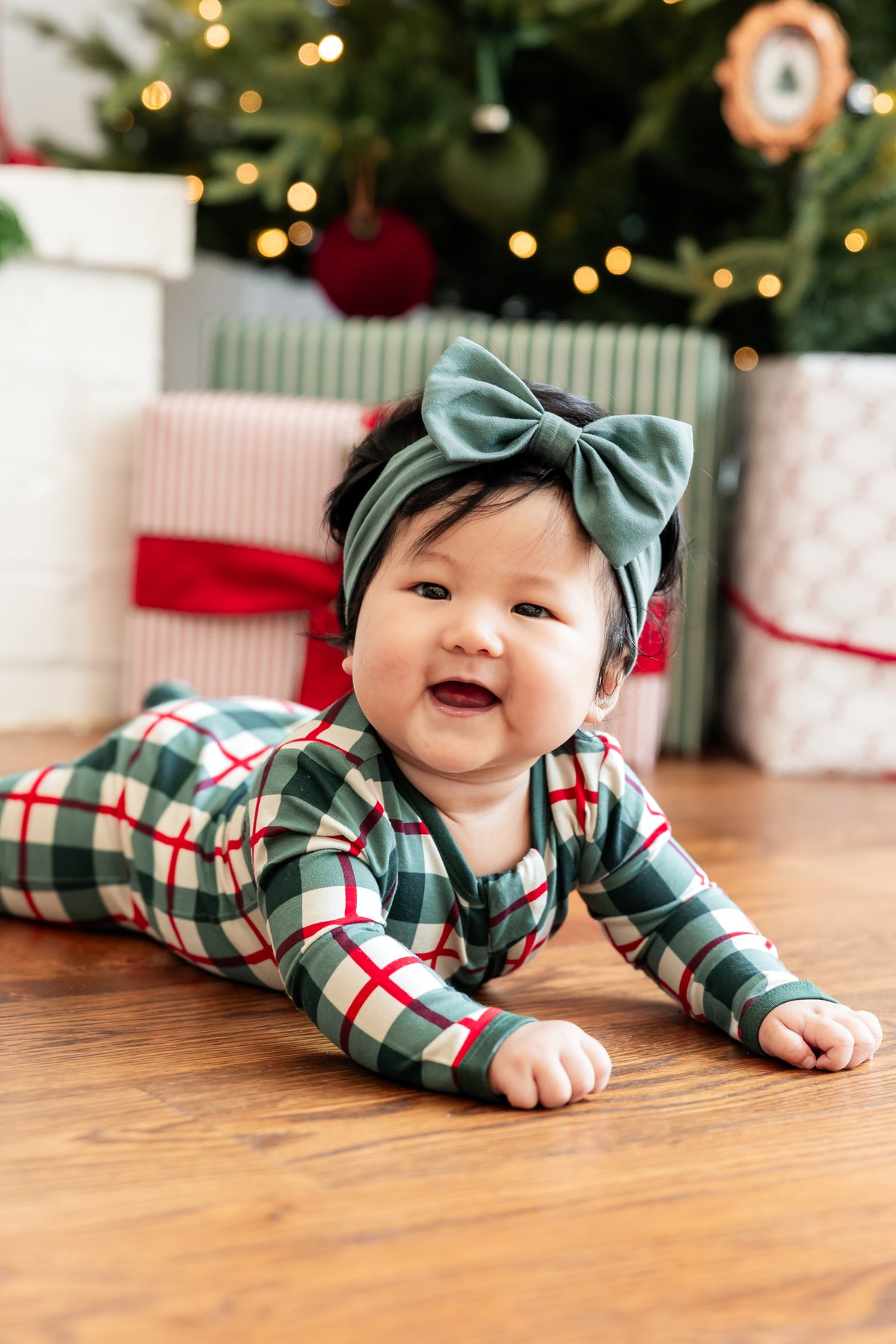 A baby footed one-piece sleeper with a green, white, and red plaid pattern, featuring a front zipper closure and long sleeves.
