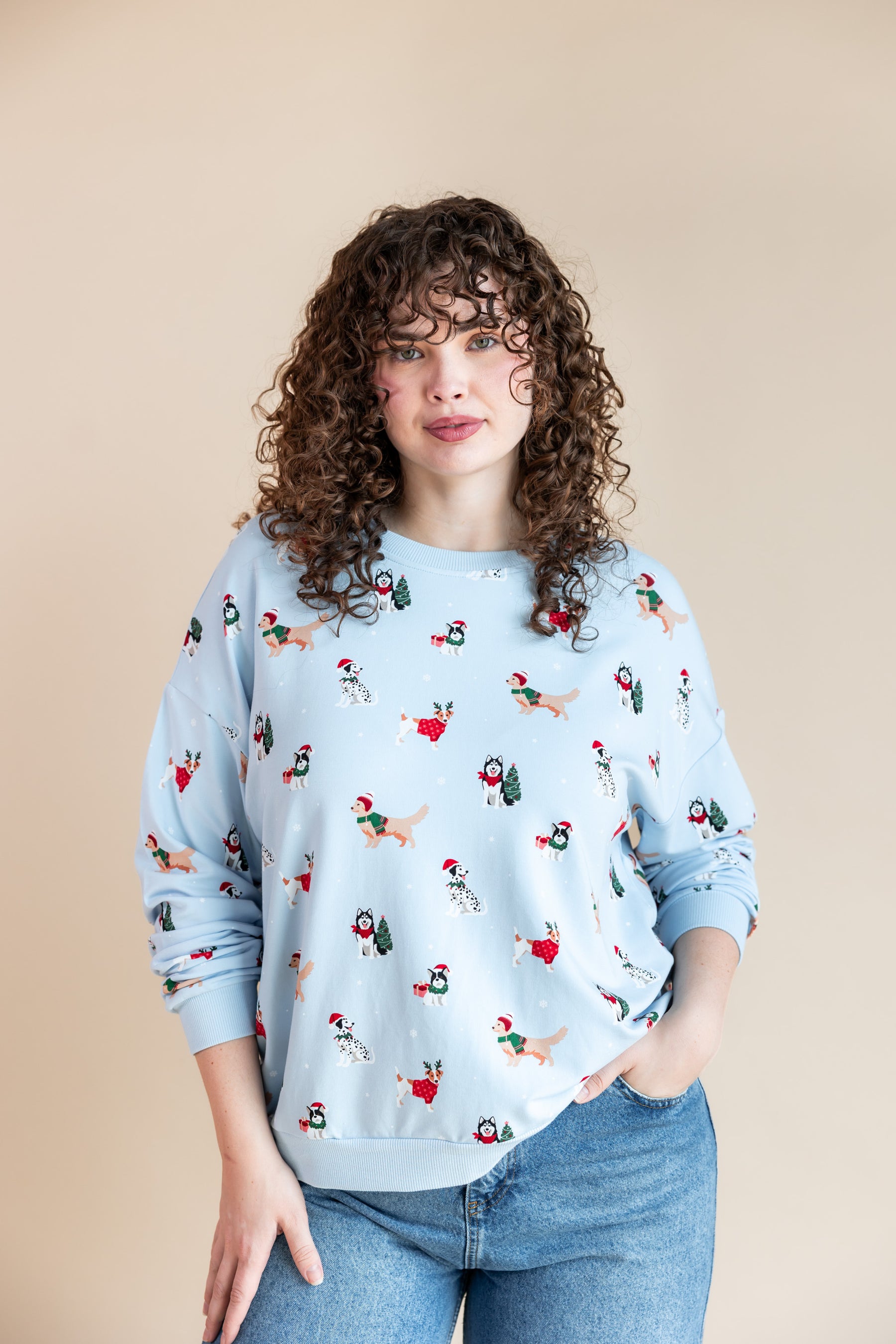 Woman wearing Women's Sweatshirt in Holiday Pups print over blue jeans on a beige background