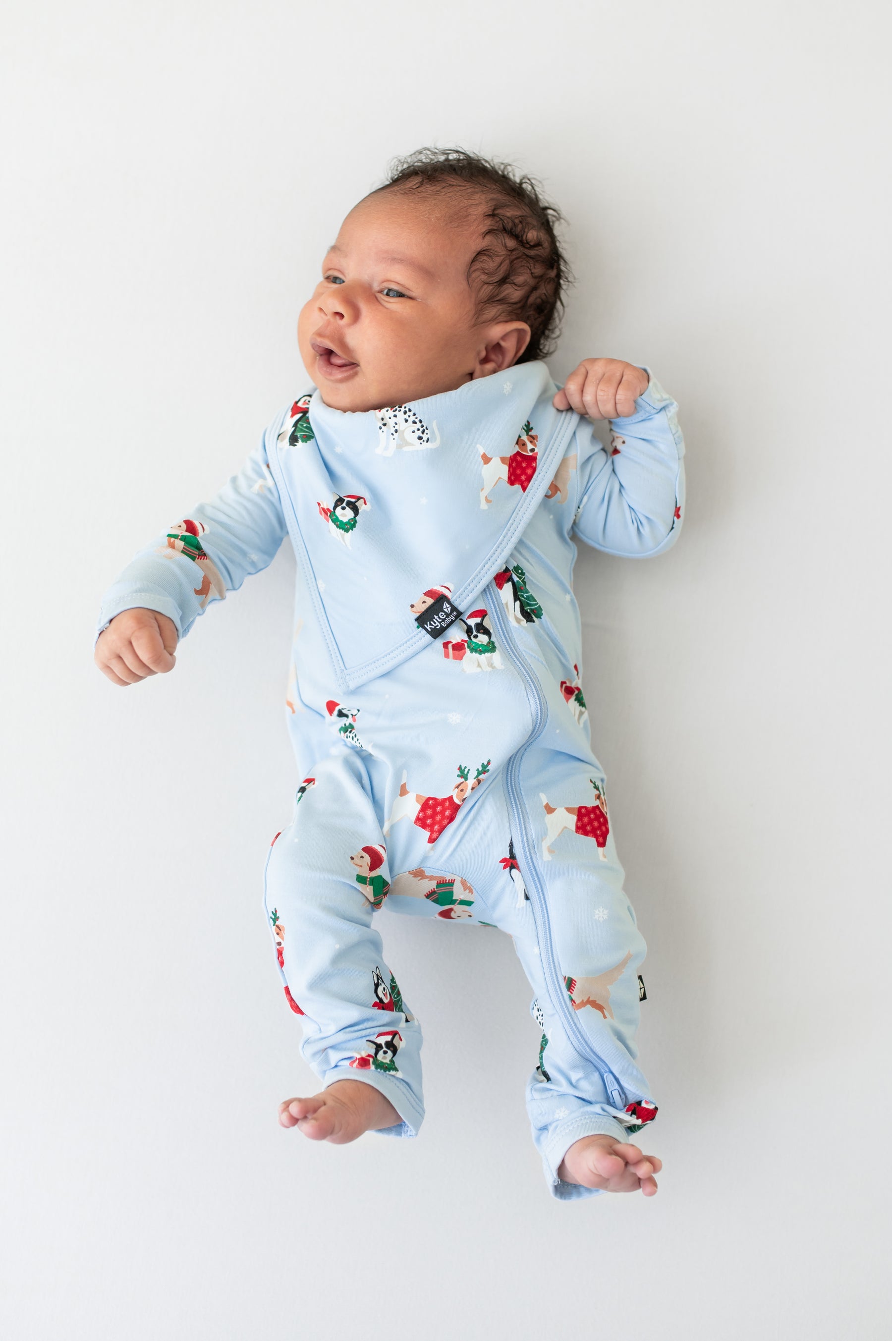Baby wearing Bib in Holiday Pups print over similar print romper on a beige background