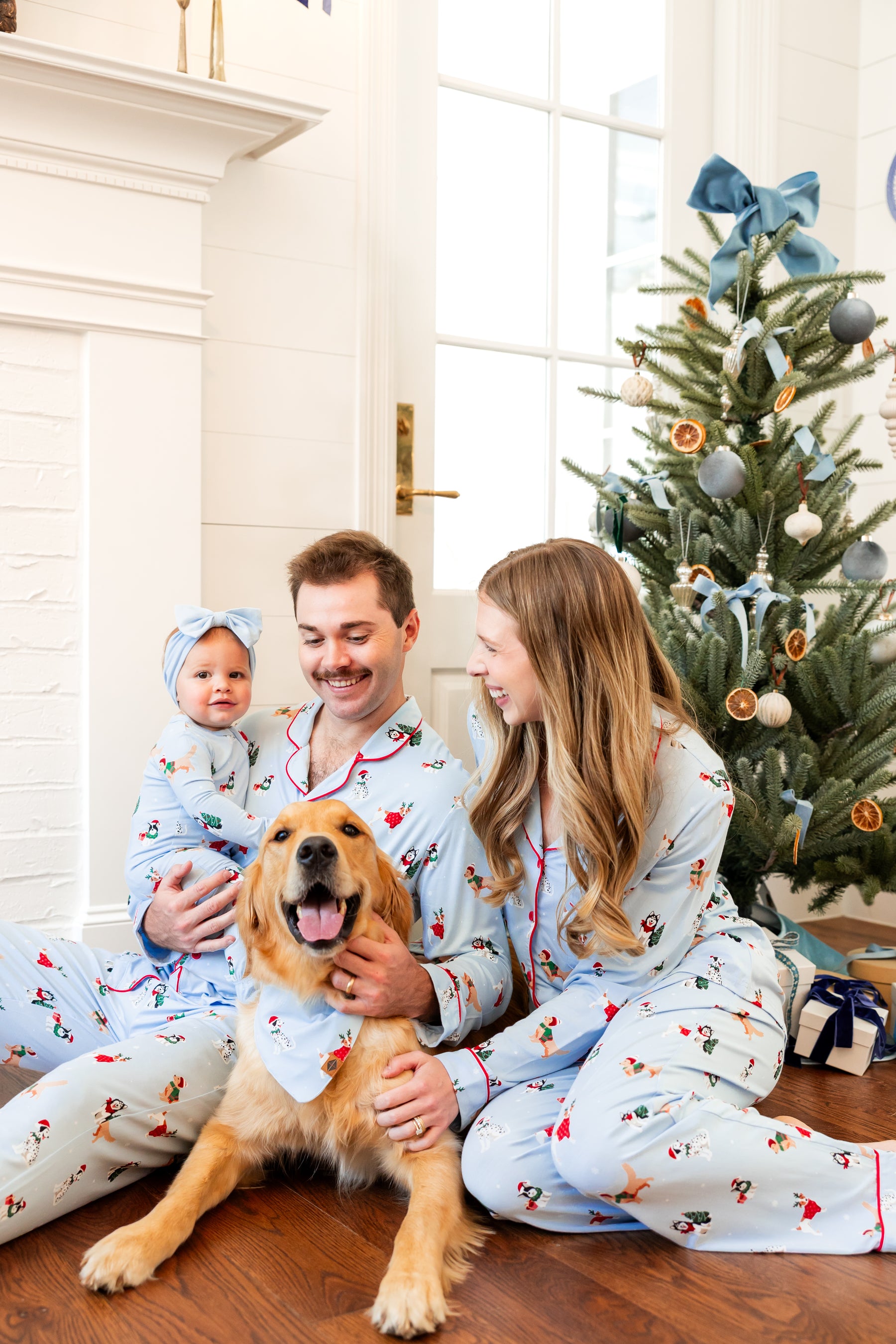 Family of 3 with a golden retriever dog wearing matching holiday puppy printed pajamas and the dog in a matching bandana 