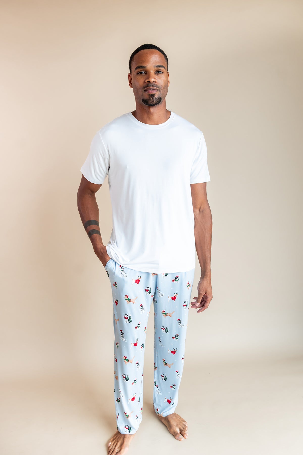 Man wearing Men's Lounge Pants in Holiday Pups print under white T-shirt on a beige background