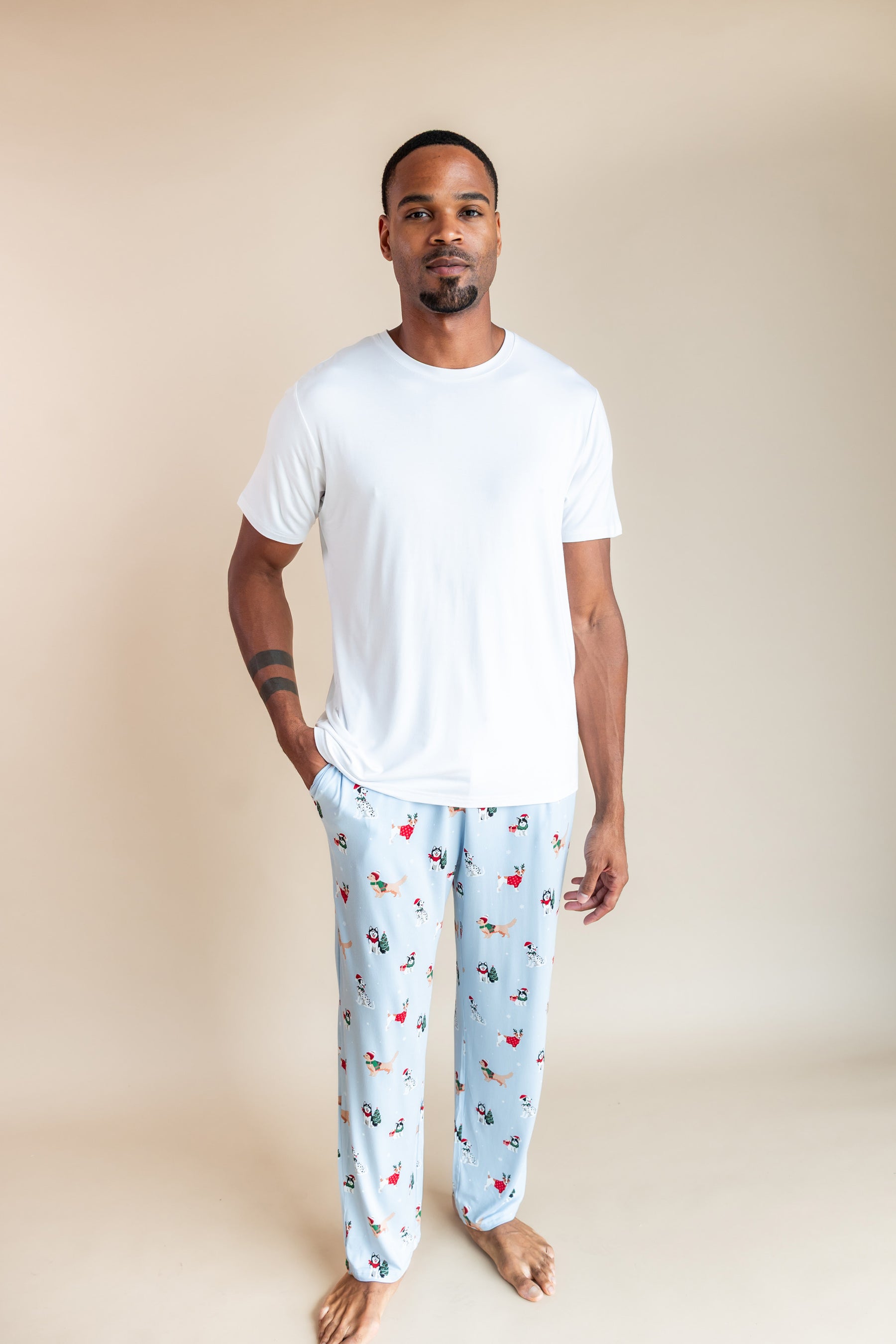 Man wearing Men's Lounge Pants in Holiday Pups print under white T-shirt on a beige background