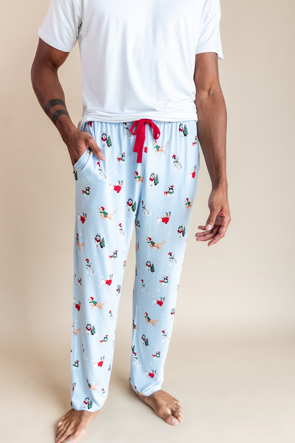 Modal wearing Men's Lounge Pants in Holiday Pups print under white T-shirt on a beige background