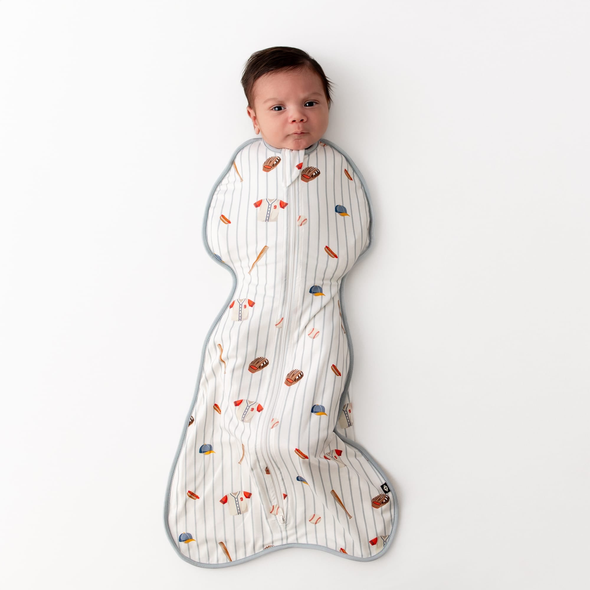 Newborn laying on a white surface wearing the Swaddle Bag in Home Run 0.5