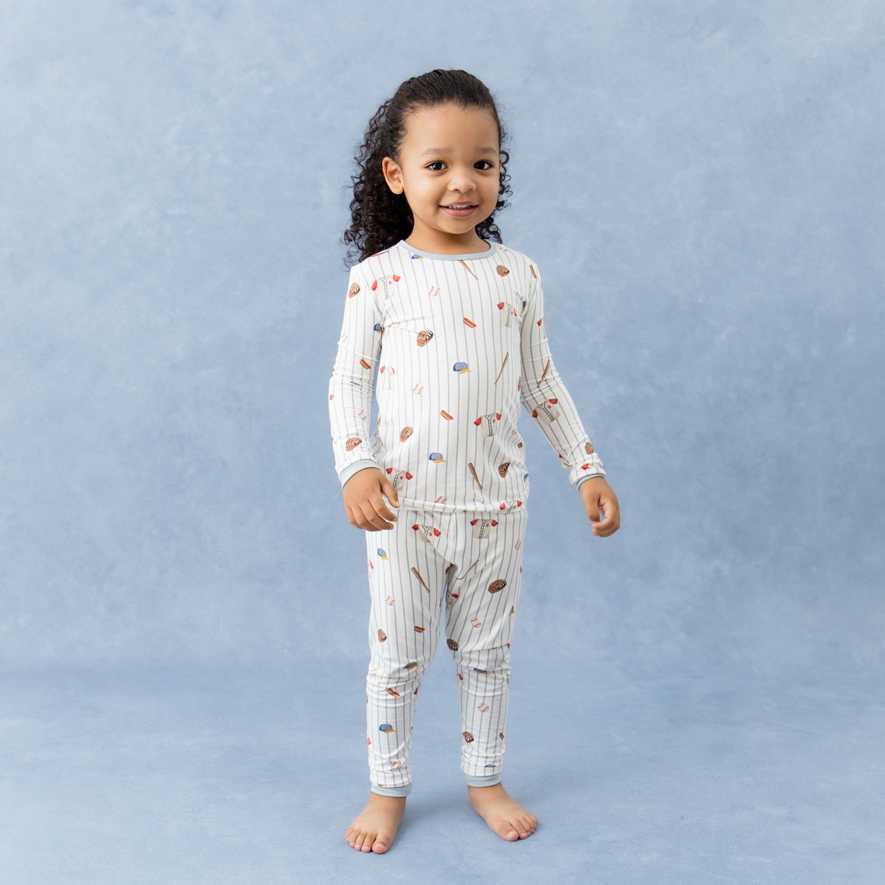 Young girl standing in front of a marbled background wearing the Long Sleeve Pajamas in Home Run