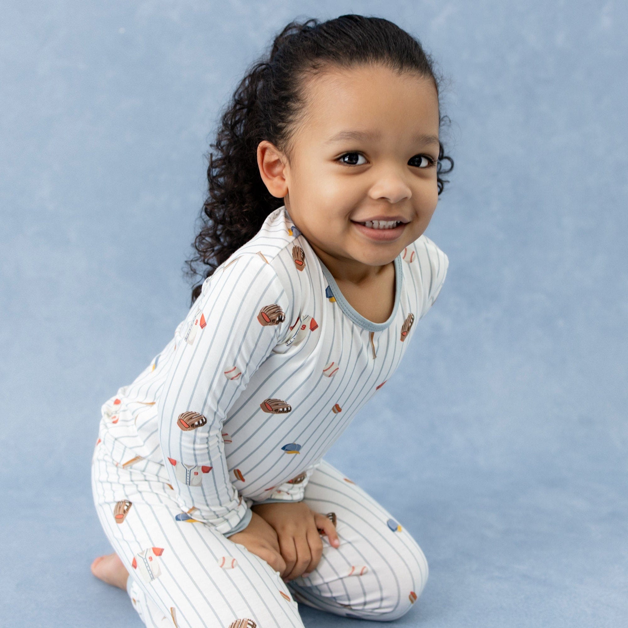 Young girl kneeling on the ground wearing the Long Sleeve Pajamas in Home Run