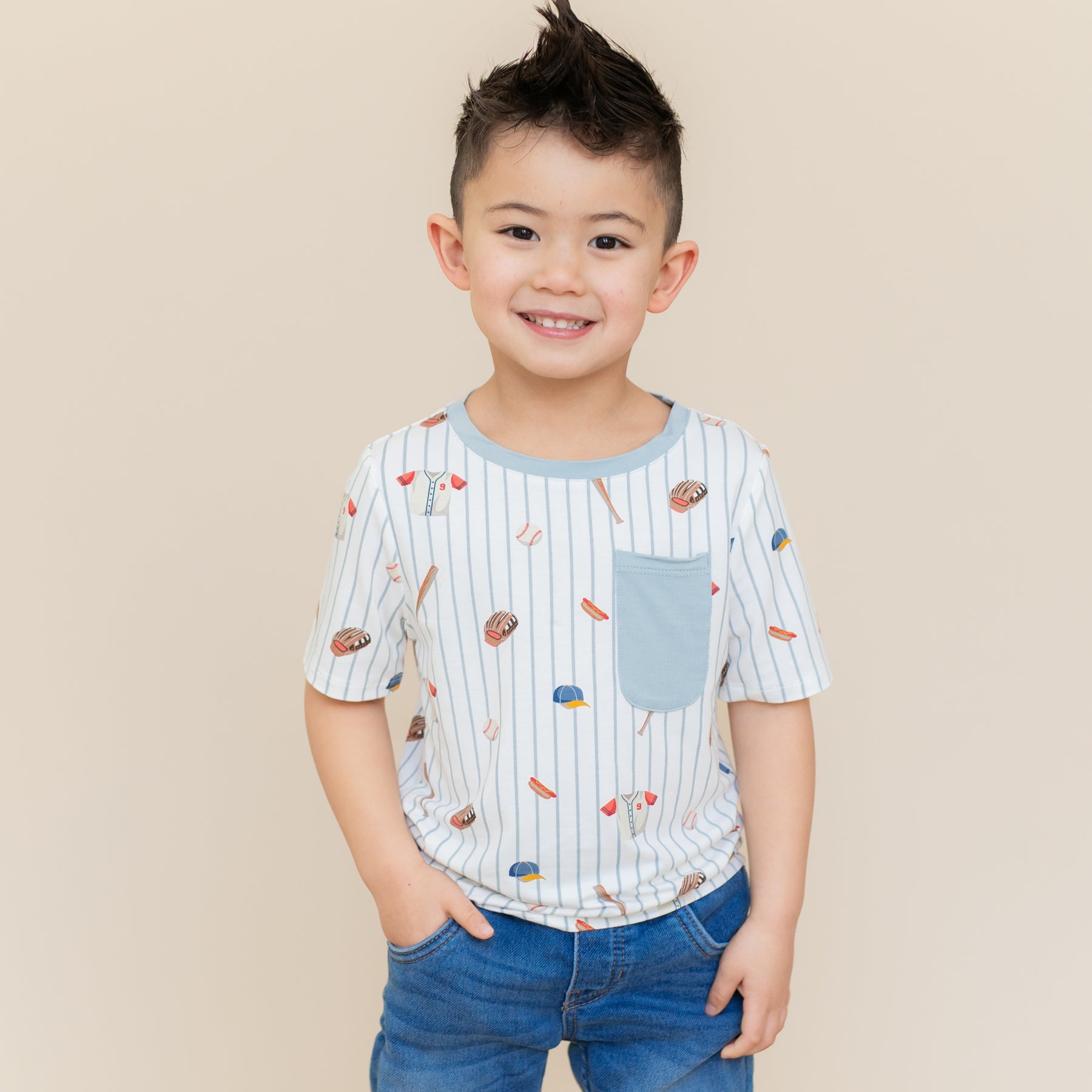 Young boy standing in front of a light beige background wearing the Toddler Crew Neck Tee in Home Run with medium wash jeans