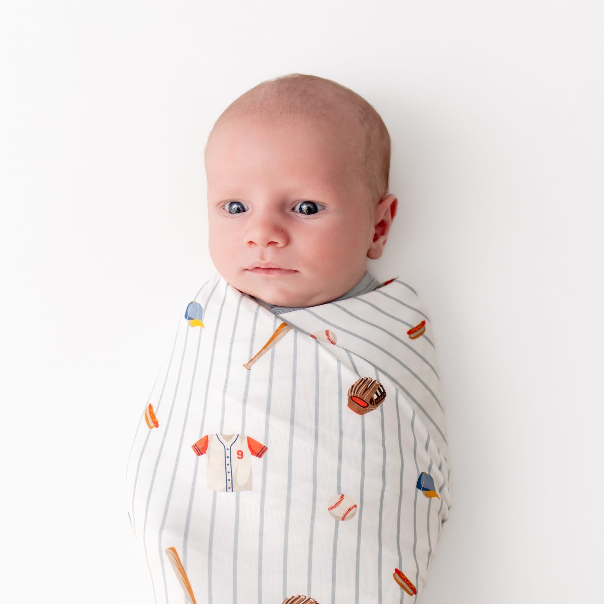 Newborn laying on a white surface swaddled in the Swaddle Blanket in Home Run