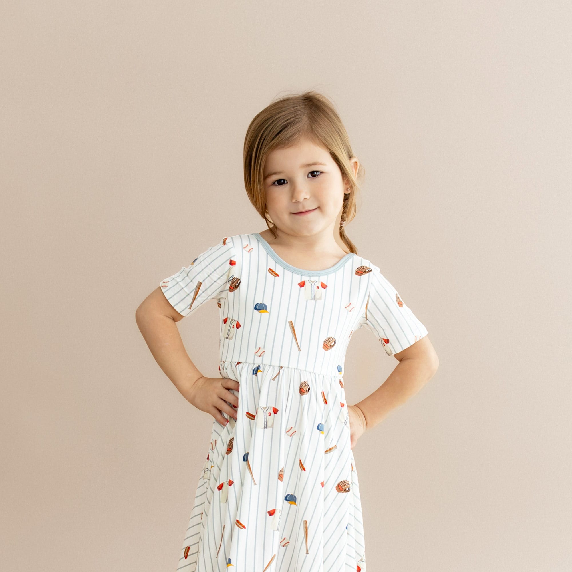 Close up of young girl wearing the Twirl Dress in Home Run with her hands on her hips
