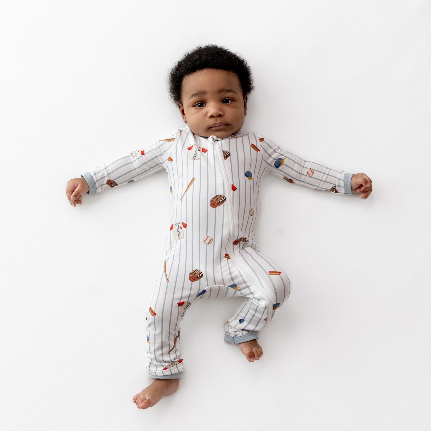 Infant lying on a white surface wearing the Zippered Romper in Home Run