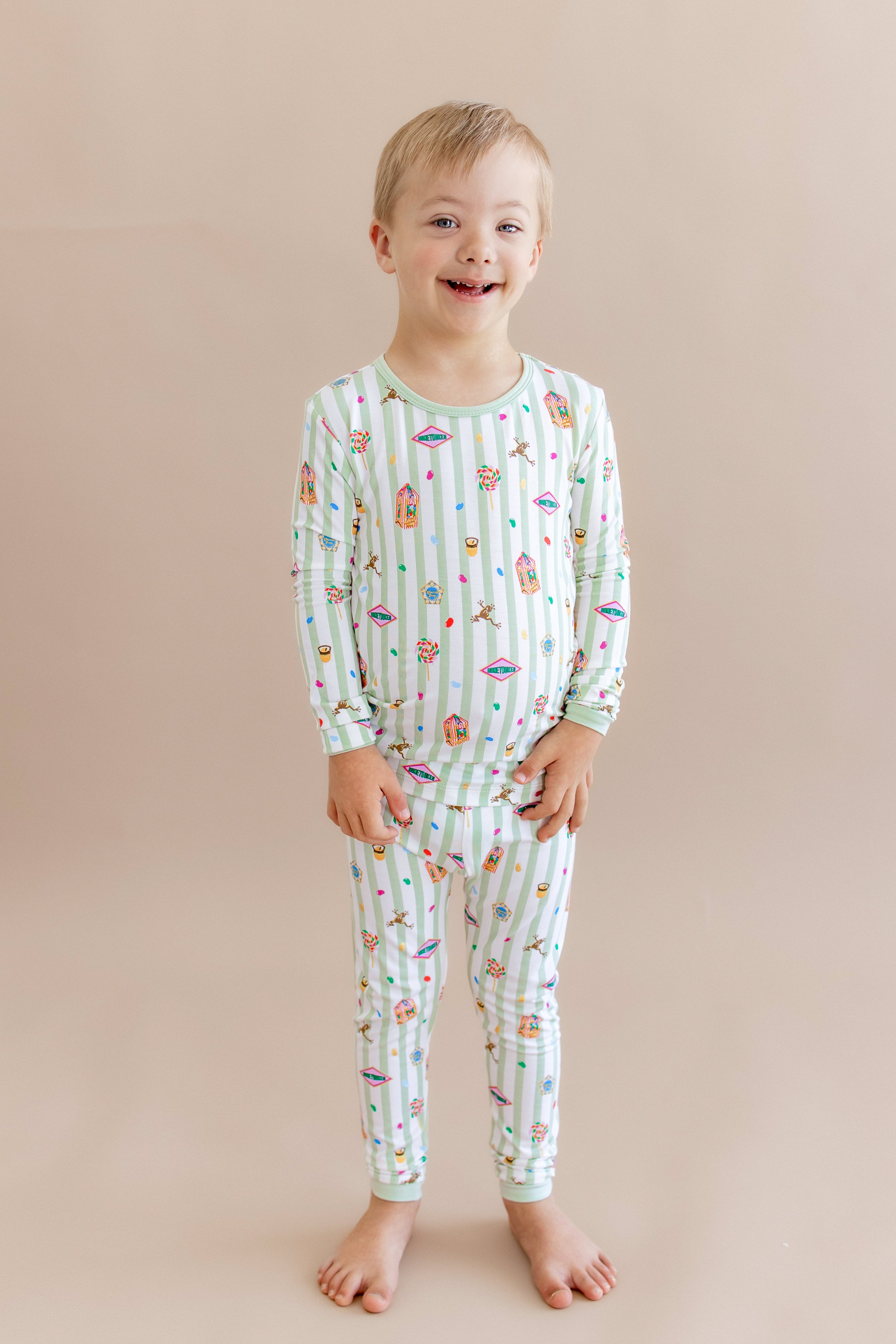 Child wearing a green and white striped long sleeve pajama set with colorful Harry Potter patterns on a beige background