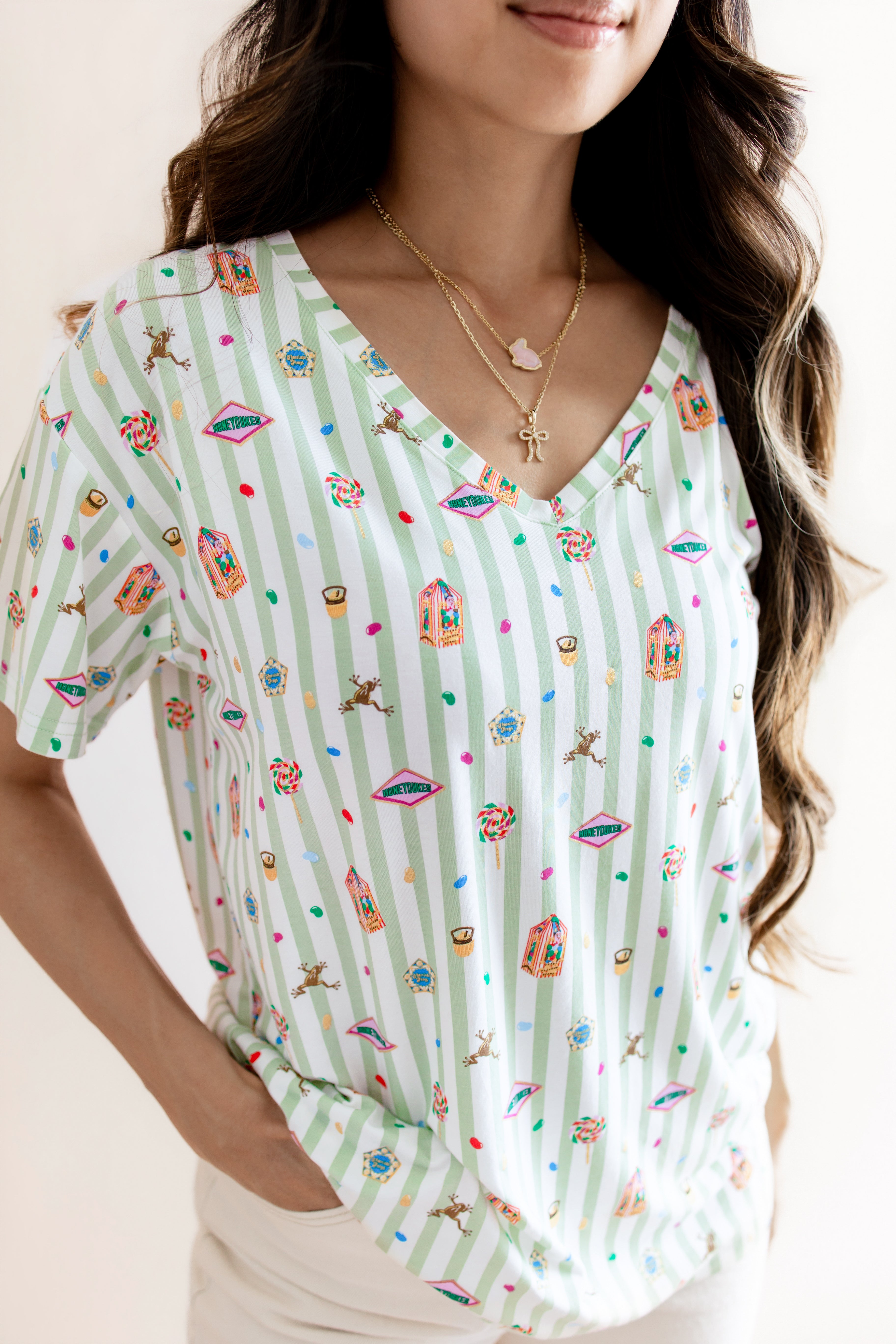 Model wearing Women's Relaxed Fit V-Neck having colorful Harry Potter patterns on a green and white striped fabric on a beige background
