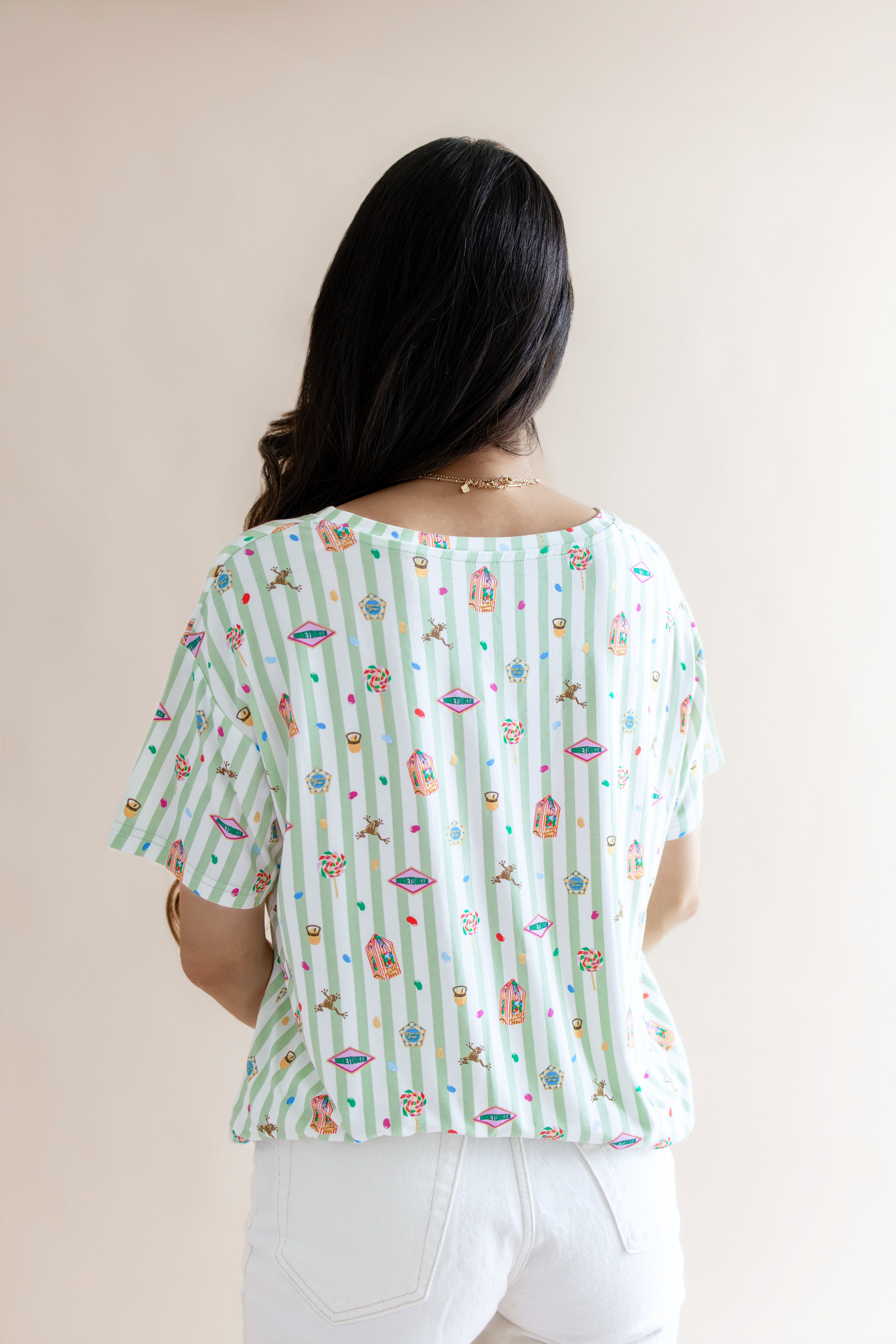 Back side of Women's Relaxed Fit V-Neck having colorful Harry Potter patterns on a green and white striped fabric on a beige background