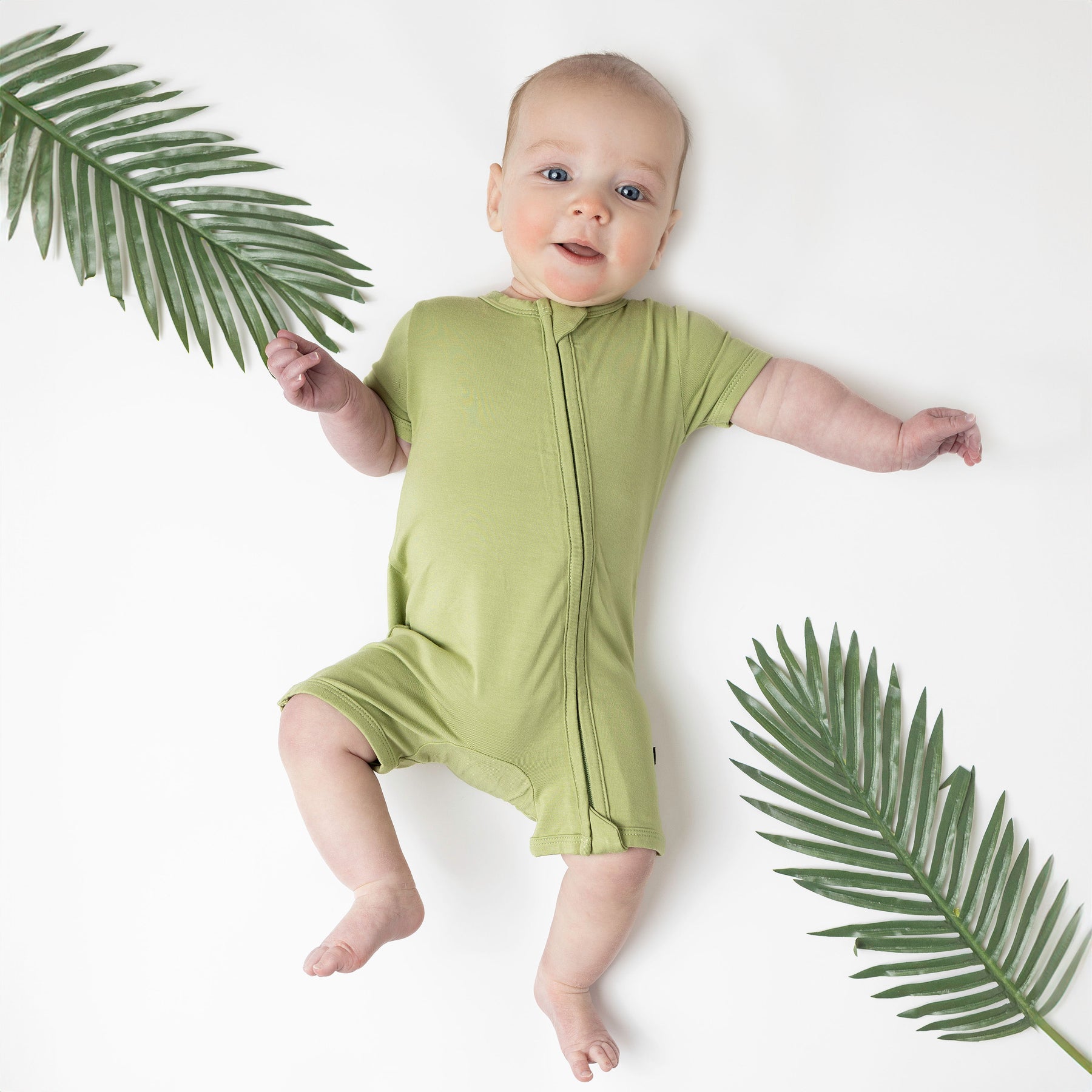 Baby in Zipper Shortall Romper in Honu with palm leaves around