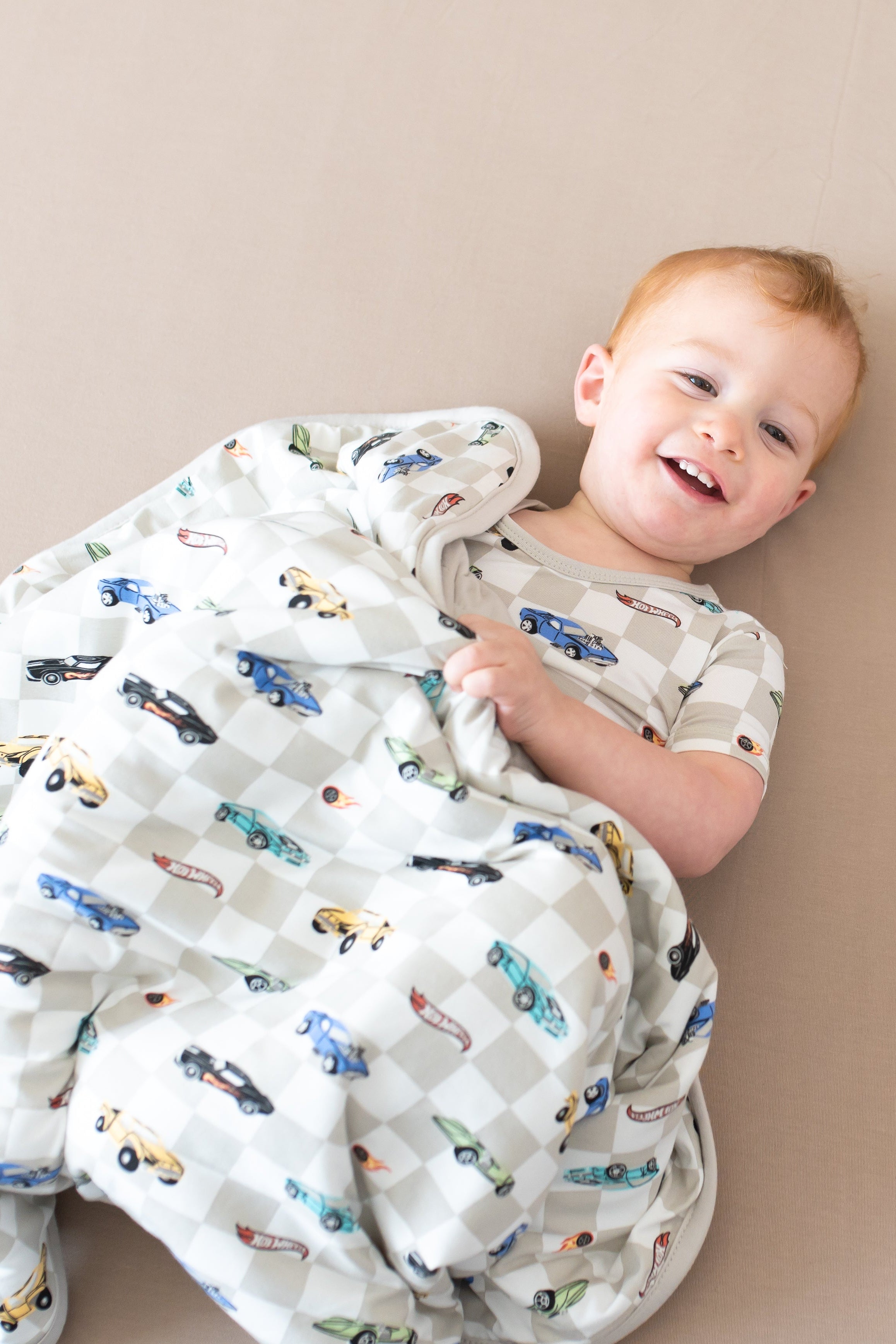 Smiling toddler laying down underneath the Baby Blanket in Fast and Fierce 1.0 wearing matching short sleeve pajamas