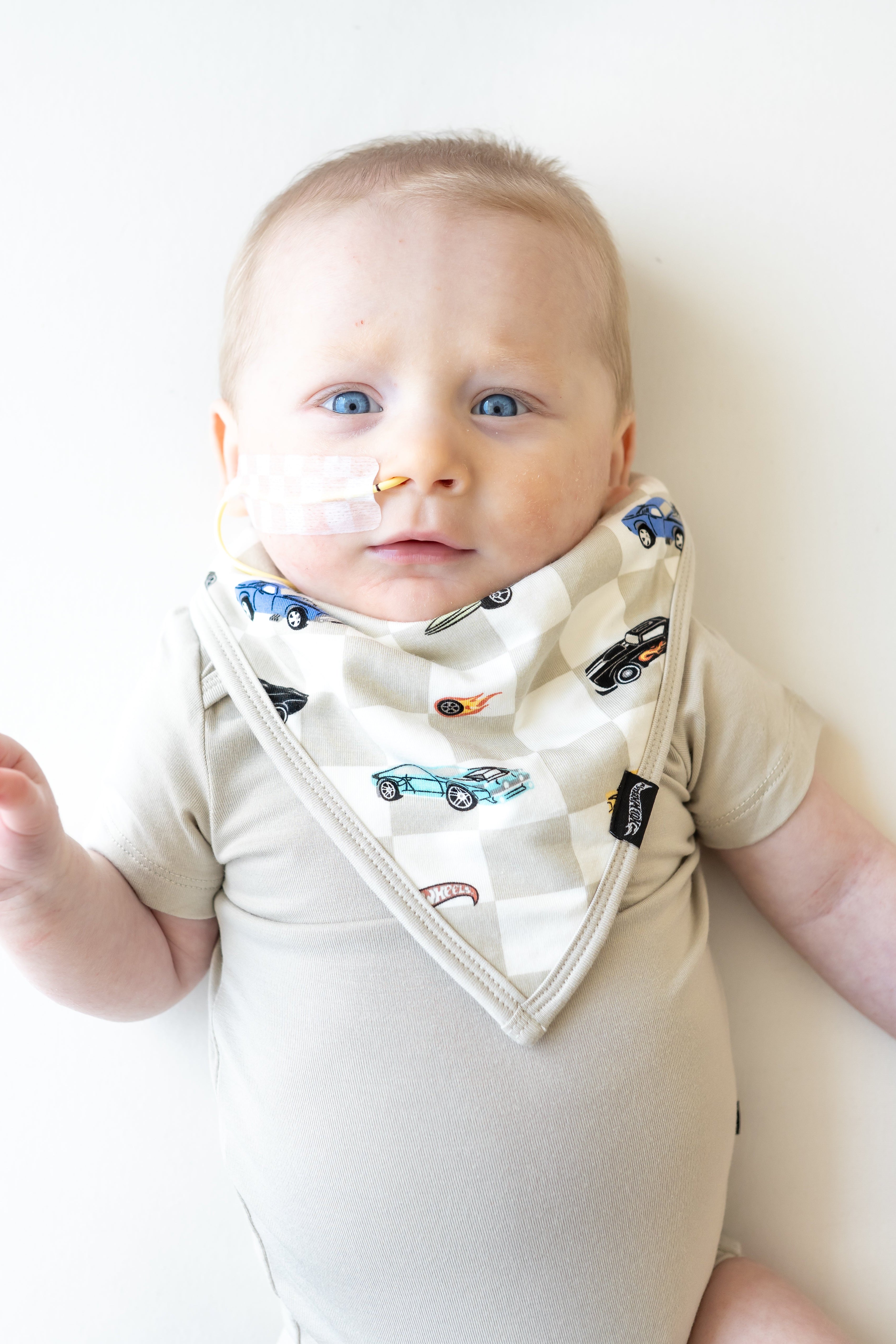 Infant laying down with one hand in the air wearing the Bib in Fast and Fierce paired with an Oat Short Sleeve Bodysuit