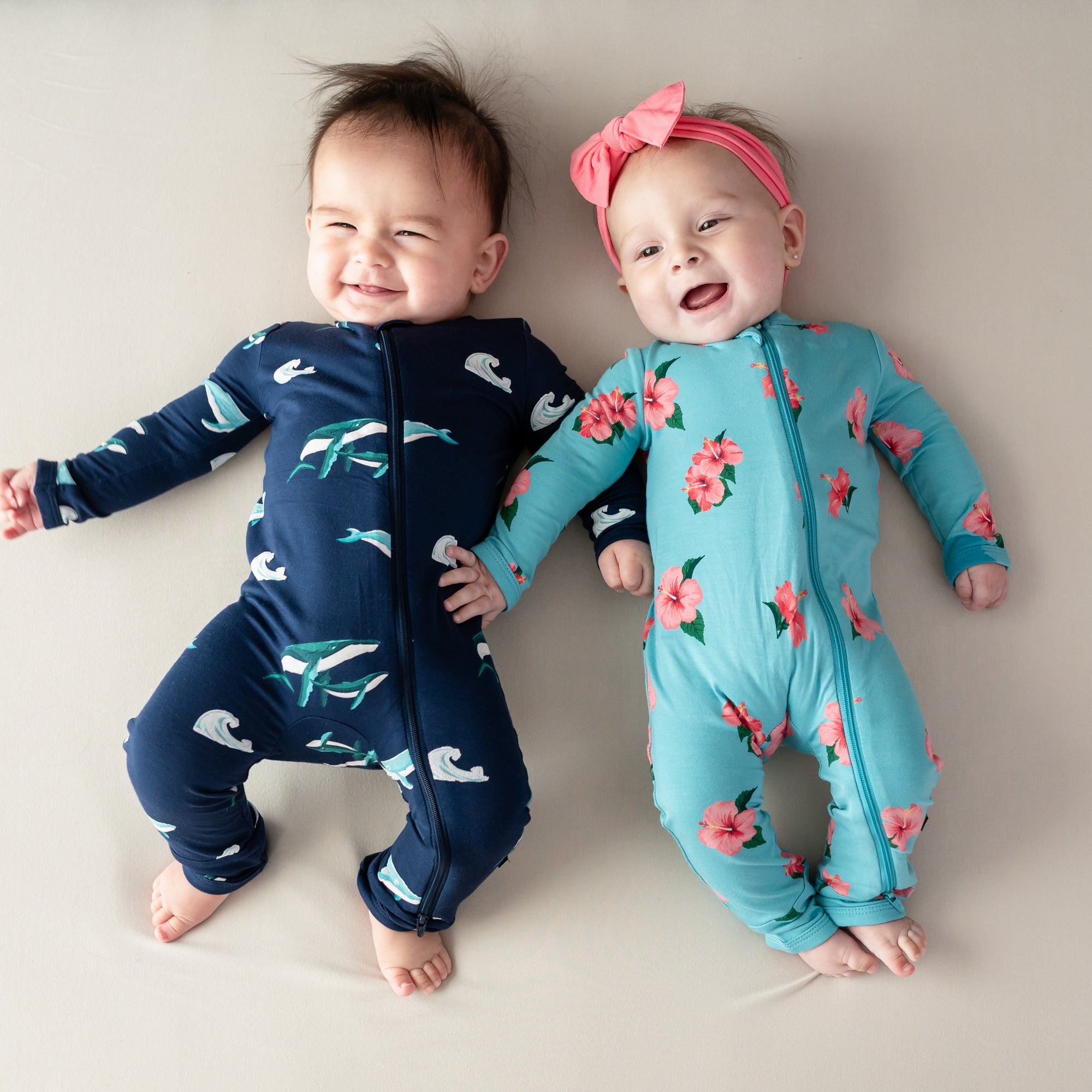 Two babies wearing Zippered Rompers from Kyte Baby in Humpback and Hibiscus 