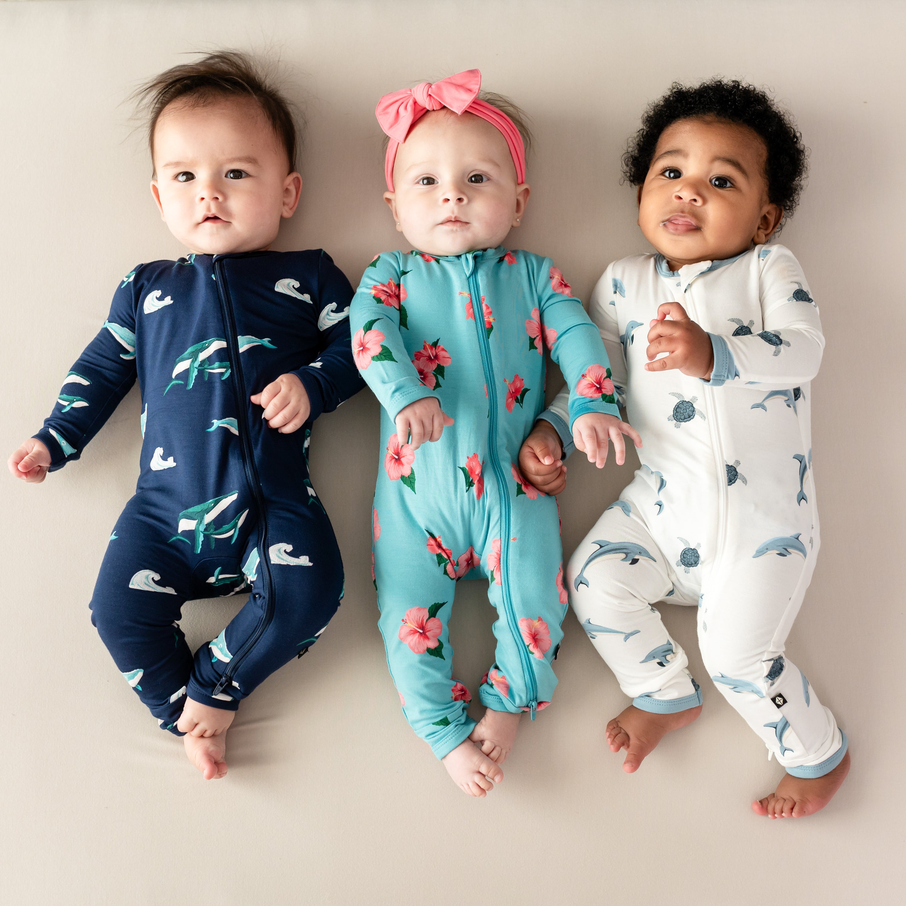 3 babies wearing Kyte Zippered Rompers in humpback, hibiscus and dolphin