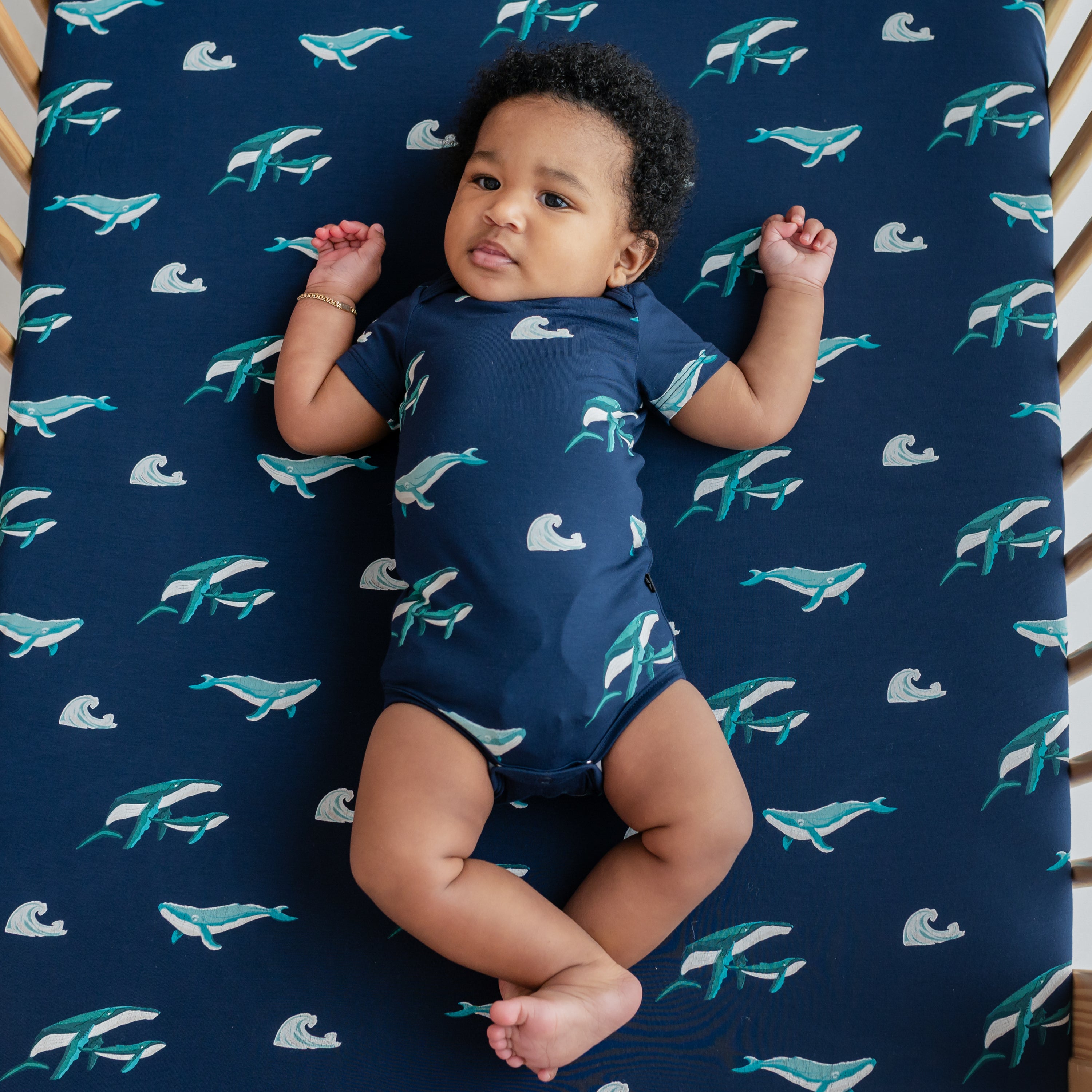 Baby wearing Bodysuit in Humpback laying in a crib with Humpback crib sheet on