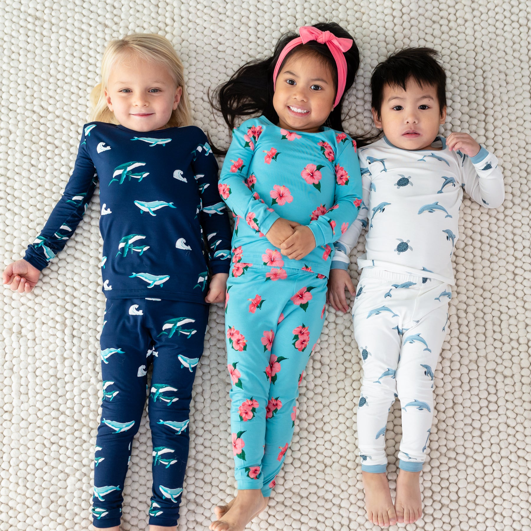 3 toddlers laying down wearing Kyte Long Sleeve Pajamas in Humpback, Hibiscus and Dolphin