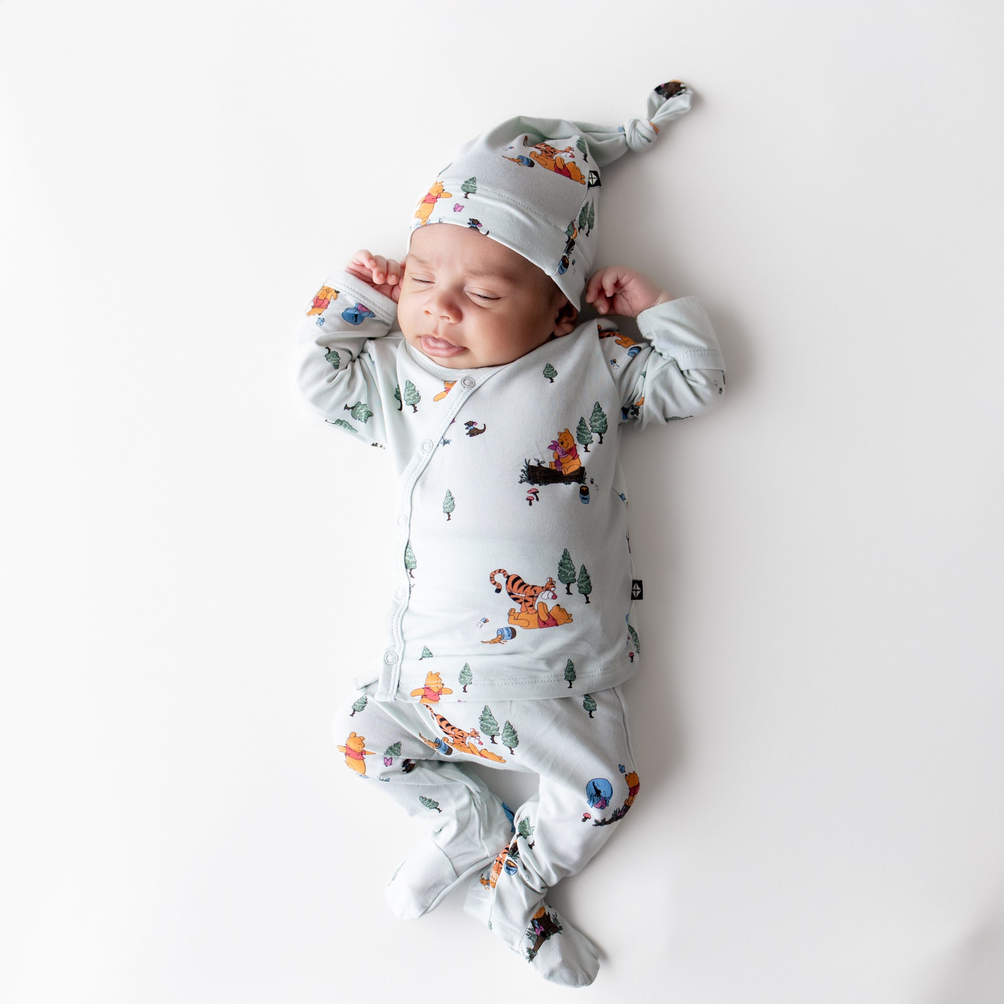 Sleeping newborn wearing the Take Me Home Set with Cap in Winnie the Pooh Hundred Acre Wood