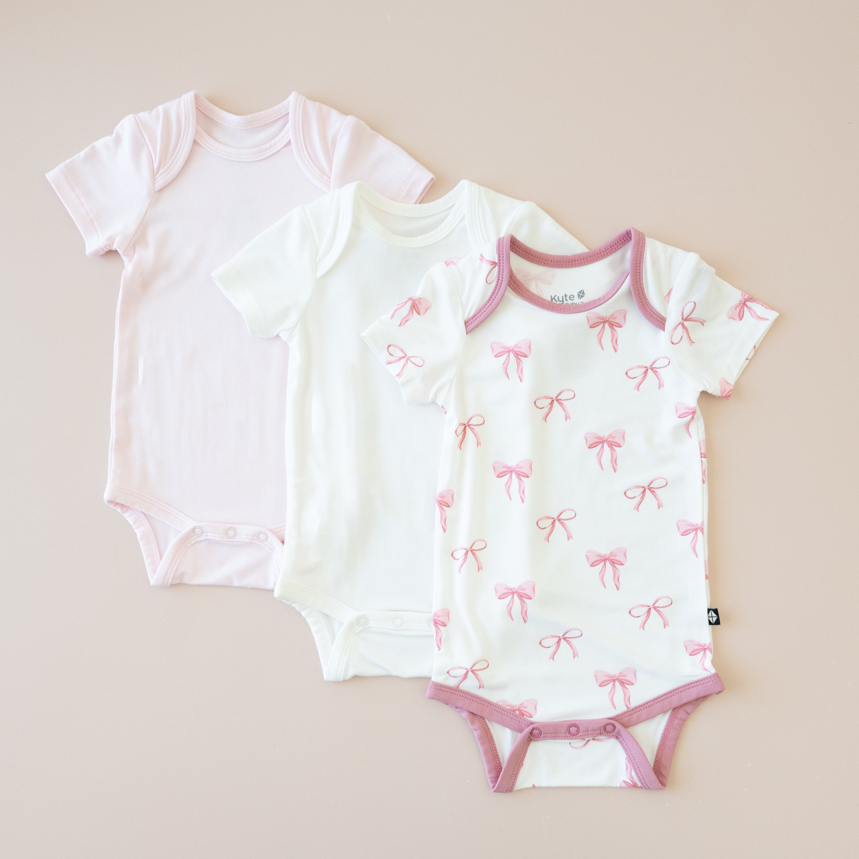Three baby bodysuits on a beige background