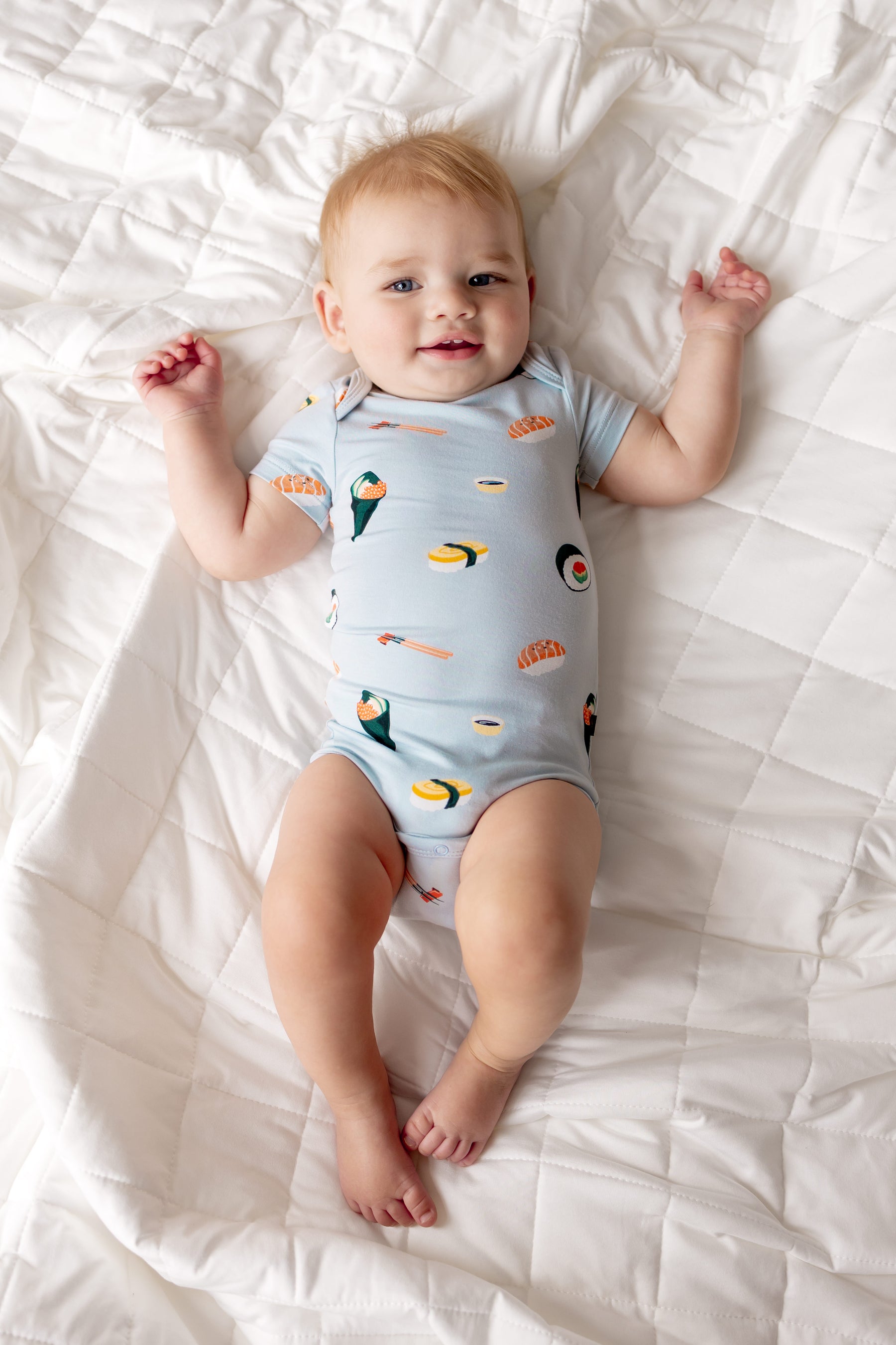 Baby lying on white sheet wearing Blue Bodysuit with Sushi print