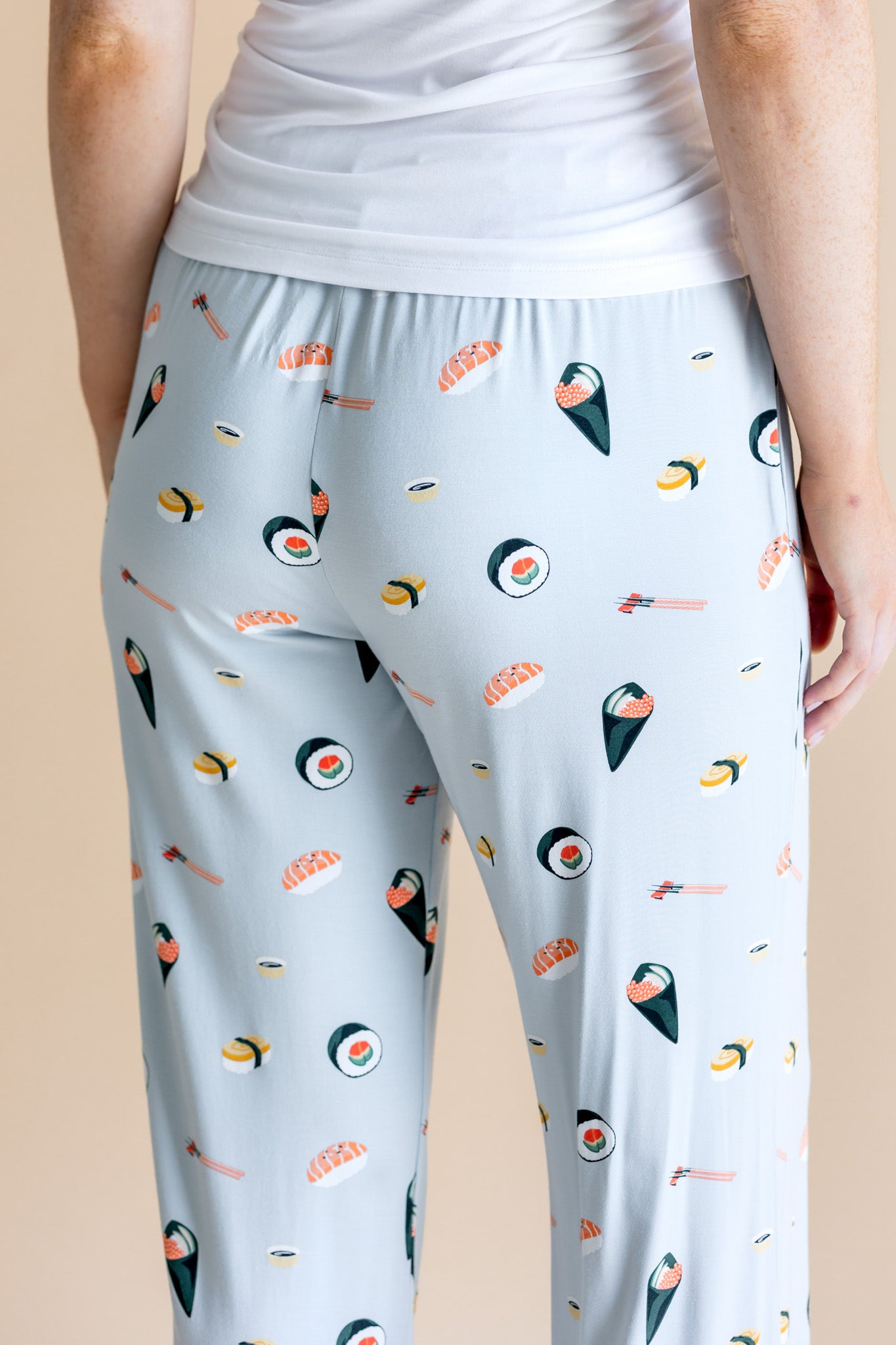 Model showing back side of blue Women's Lounge Pants in Sushi print under white camisole on a beige background